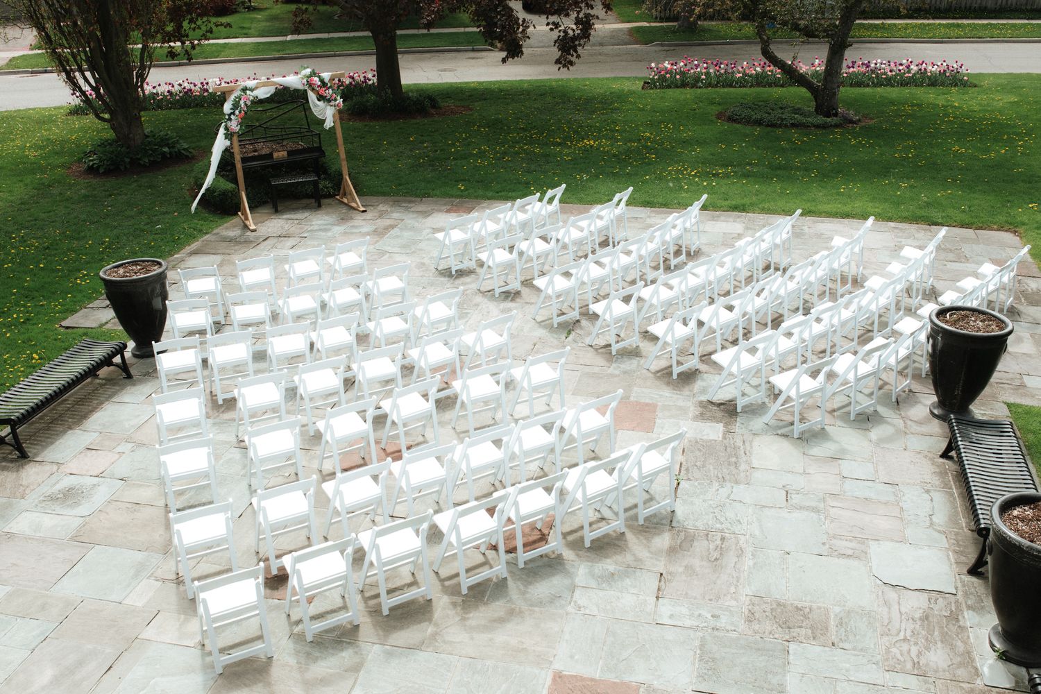 Rows of white folding chairs arranged outdoors on a stone patio for an elegant garden ceremony.