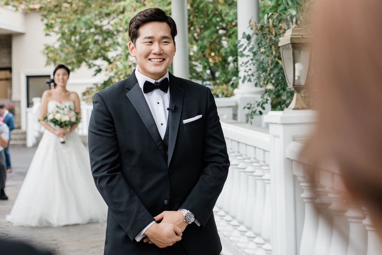 A happy couple celebrates their wedding day outdoors in formal attire with elegant white decor and greenery.