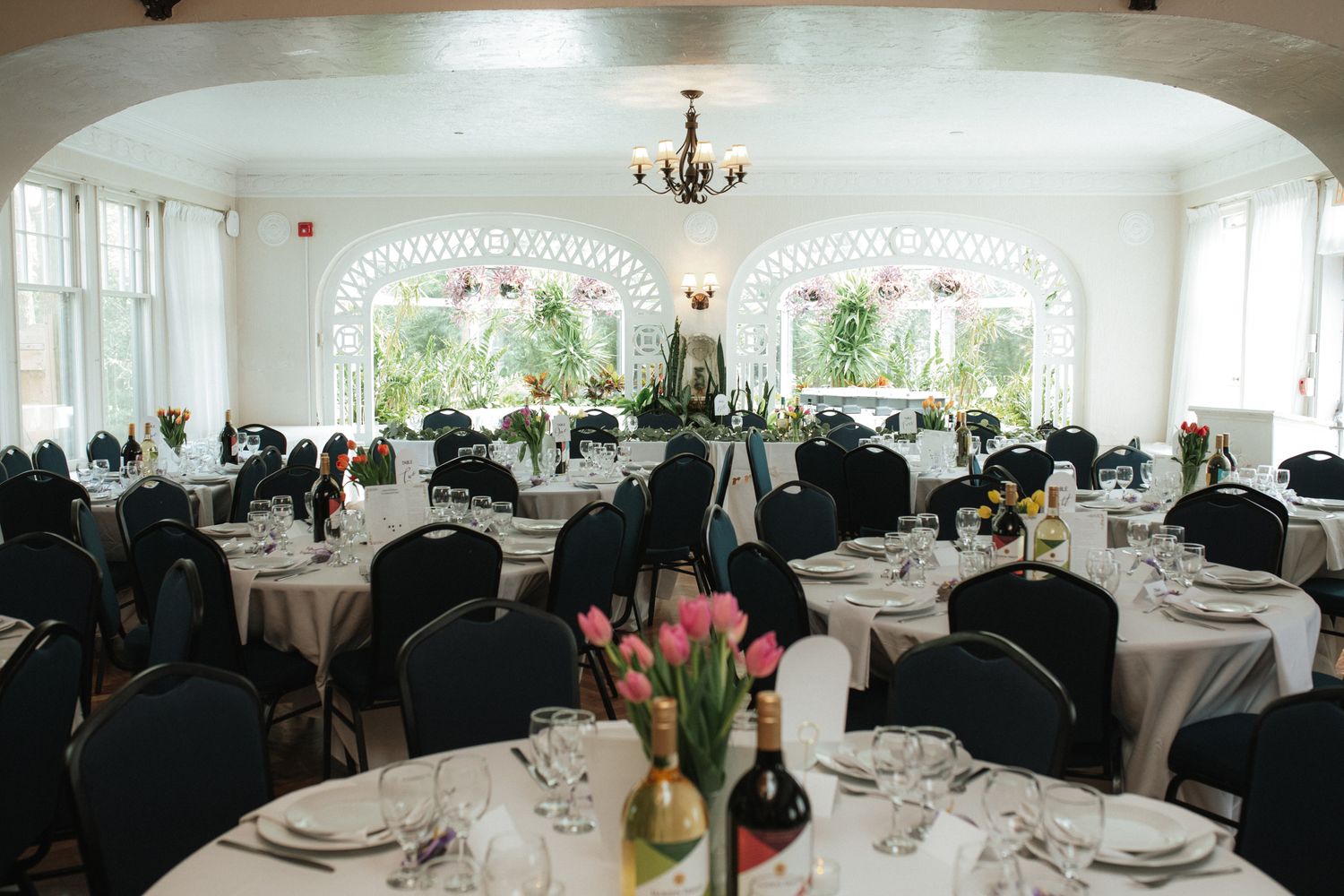 An elegant white reception hall decorated with chandeliers and tables set for a formal dining event.