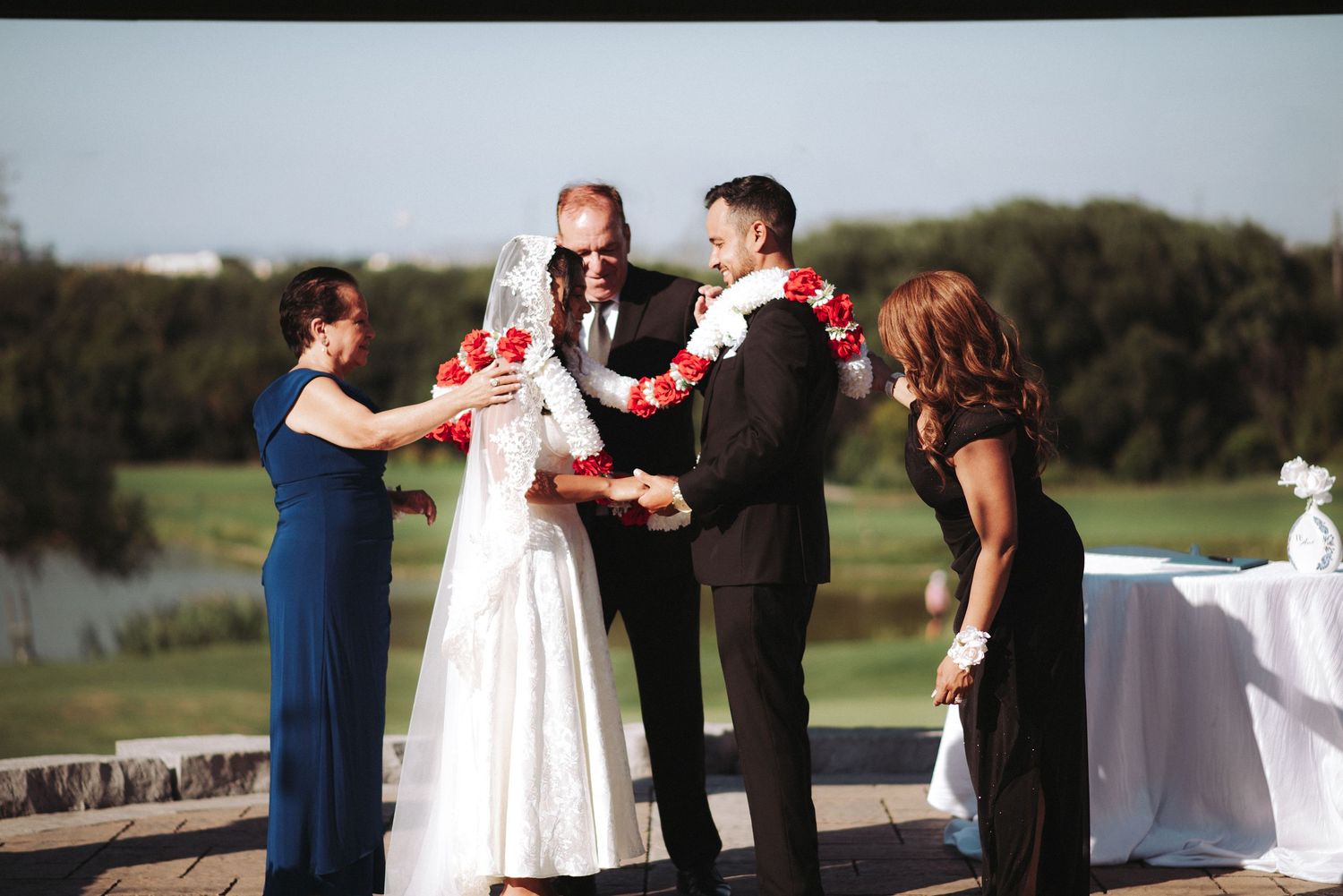 A wedding ceremony takes place outdoors with the wedding party gathered on a sunny day.