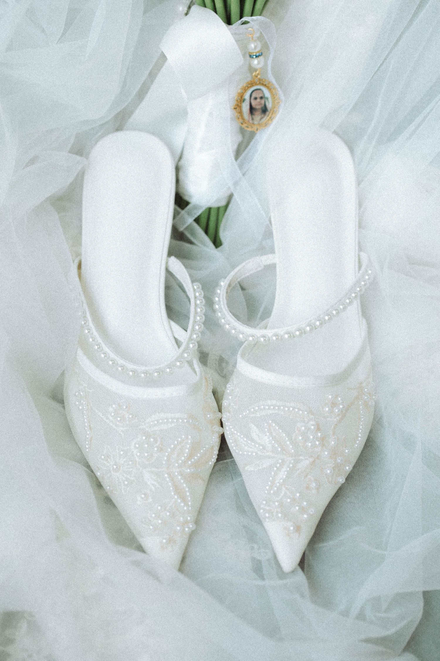 Elegant white beaded bridal shoes displayed on delicate tulle fabric with decorative embellishments.