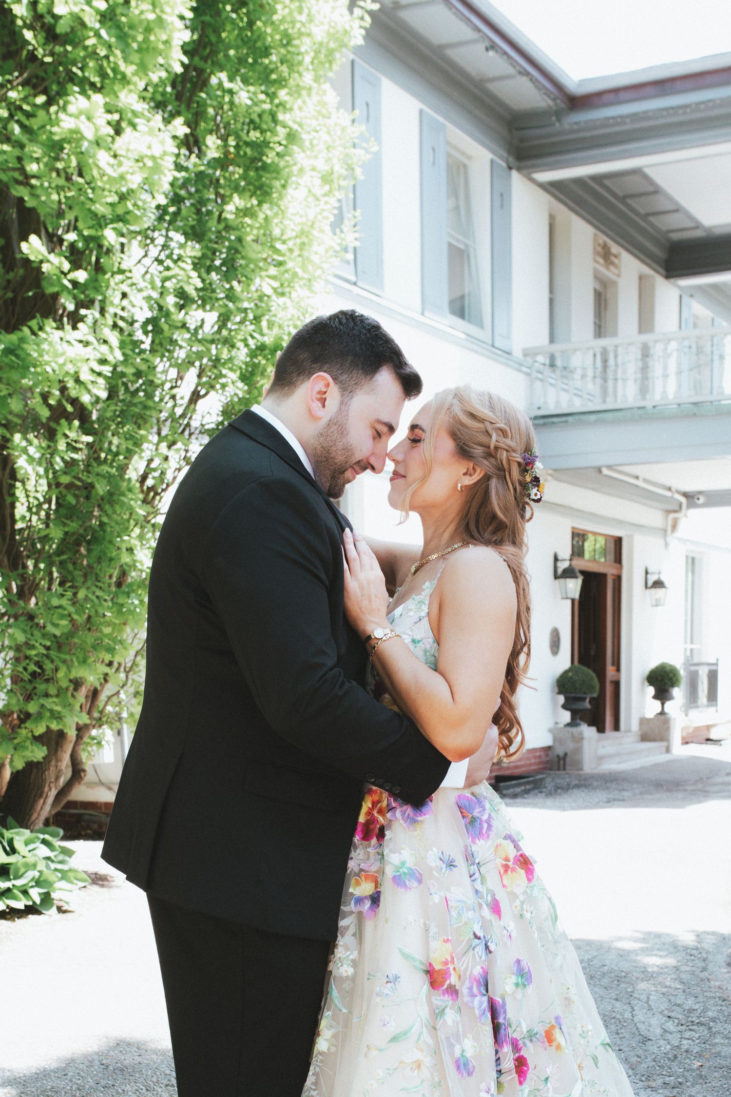 A romantic wedding couple shares tender kisses in a series of outdoor portraits by a white building.