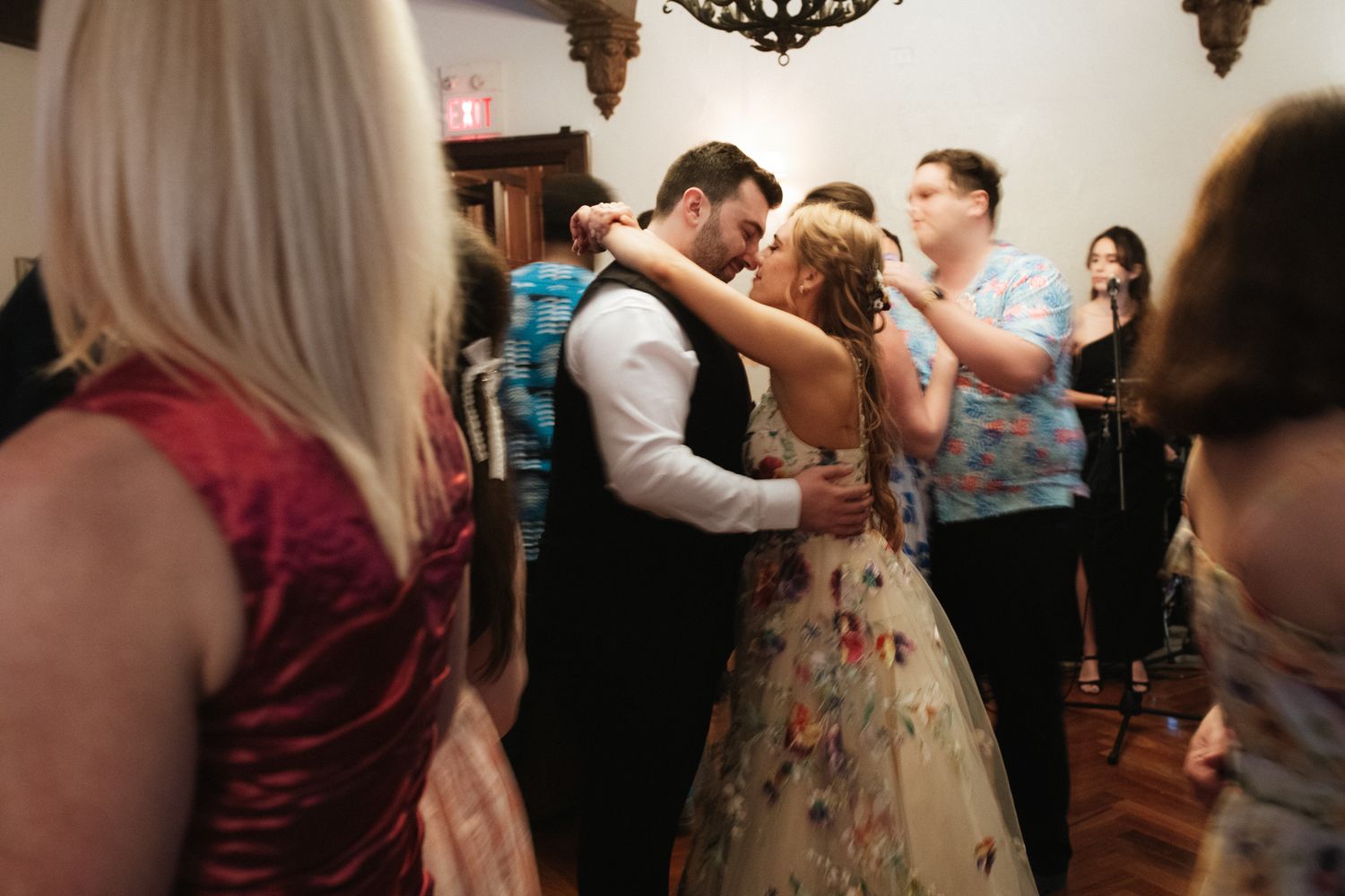Wedding guests dance and celebrate together on a dimly lit dance floor during an evening reception.