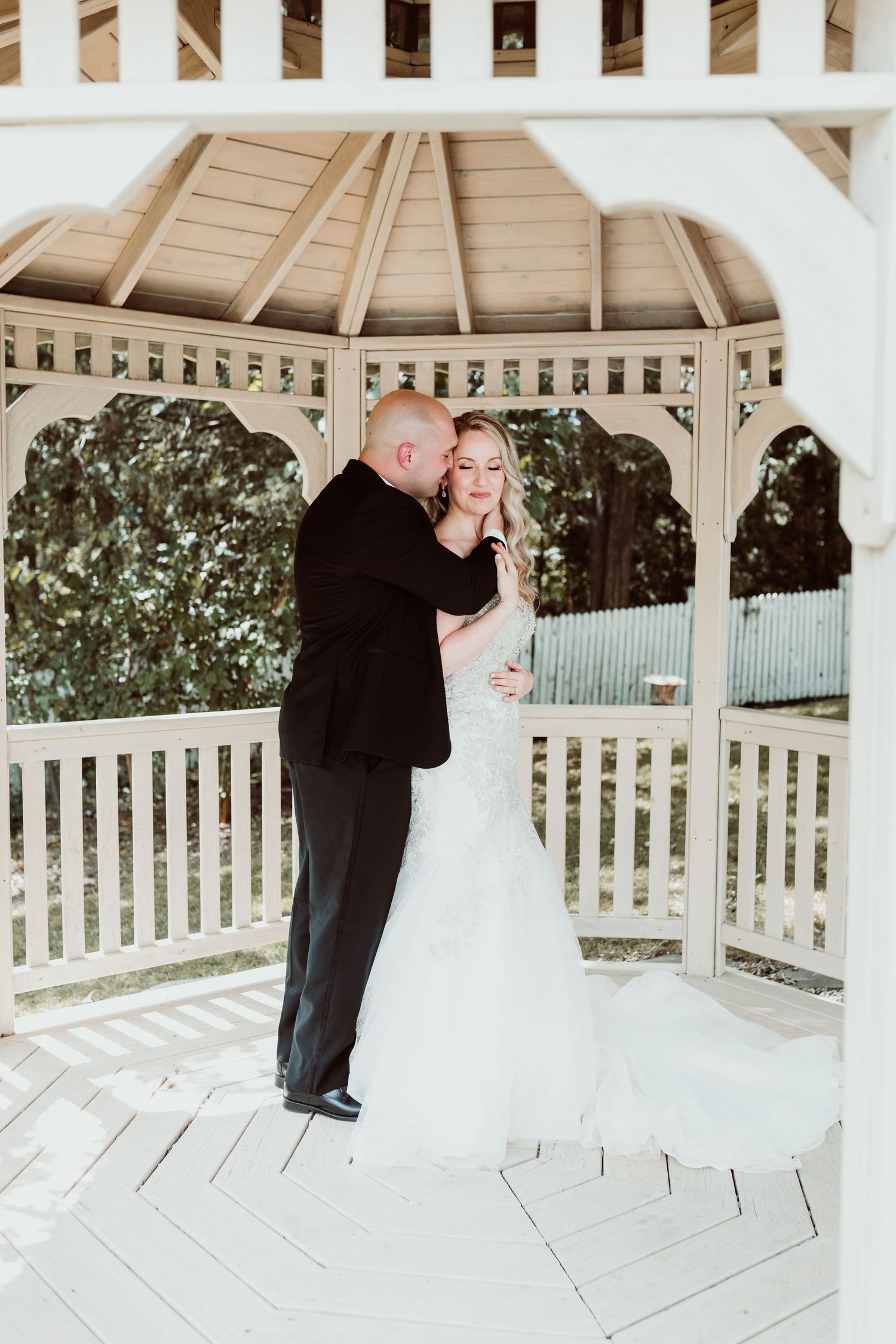 A romantic wedding couple shares a tender moment in a white wooden gazebo during their first look.