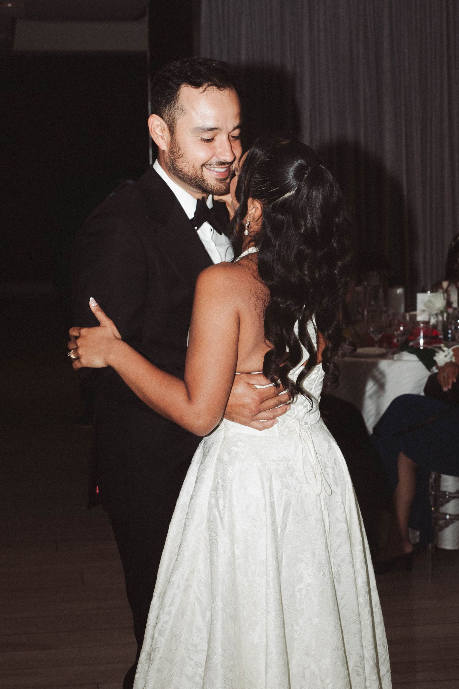 A couple shares an intimate dance at a wedding reception, with the bride wearing a white strapless gown.