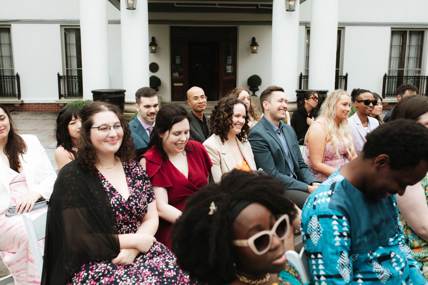 A diverse group of people sitting together at an outdoor event wearing colorful spring attire and sunglasses.