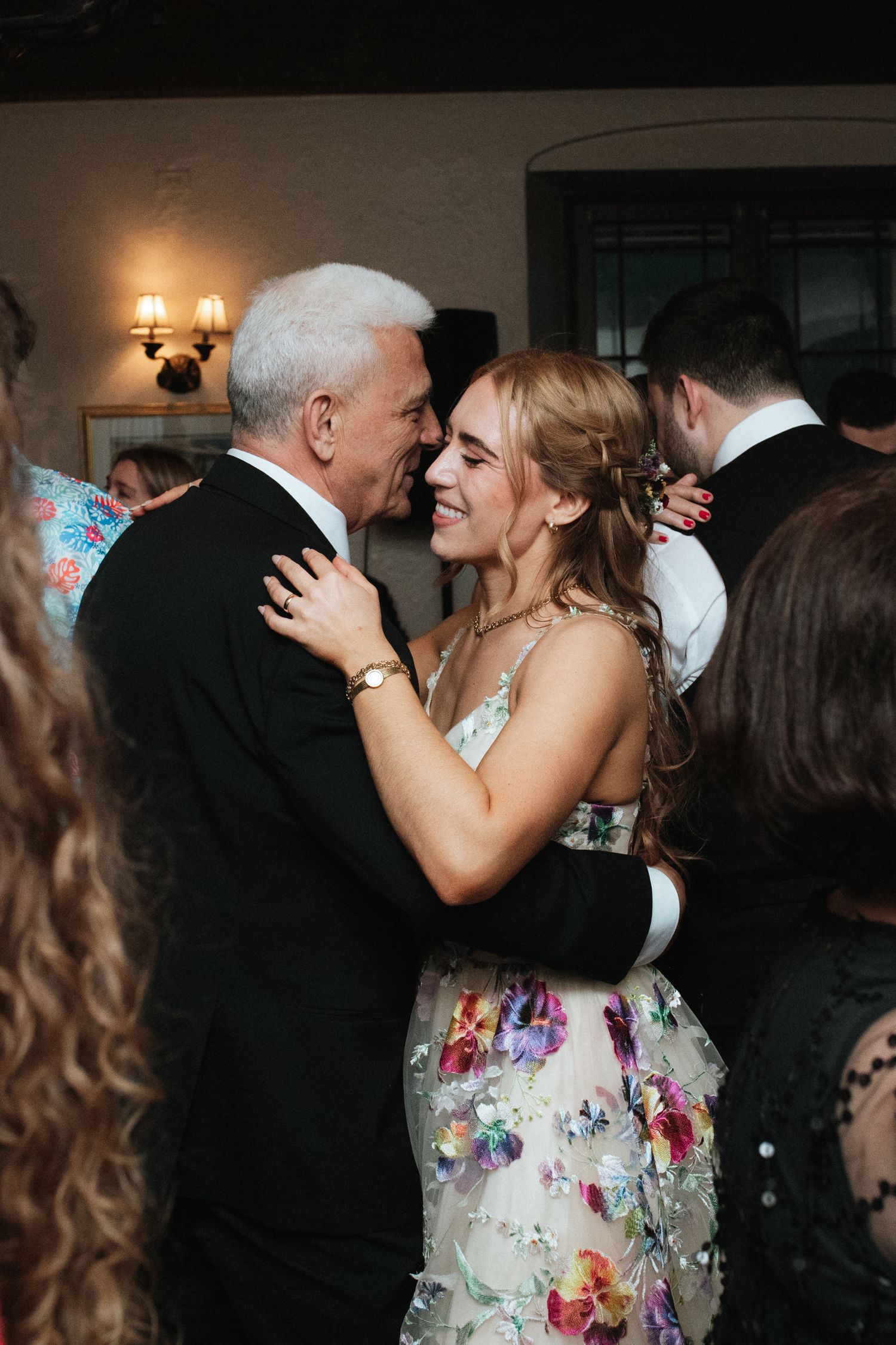 A tender moment between a bride in a floral dress and her dance partner during a wedding reception.