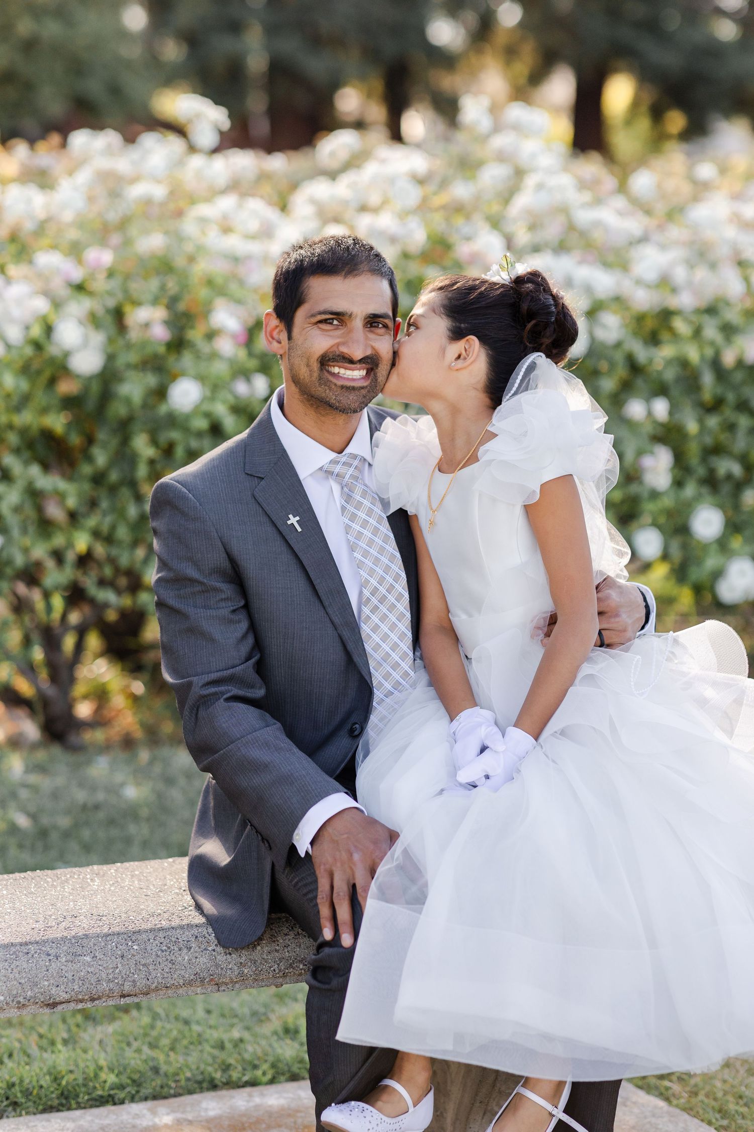 A couple shares a tender moment on their wedding day in a garden with white flowers in the background.