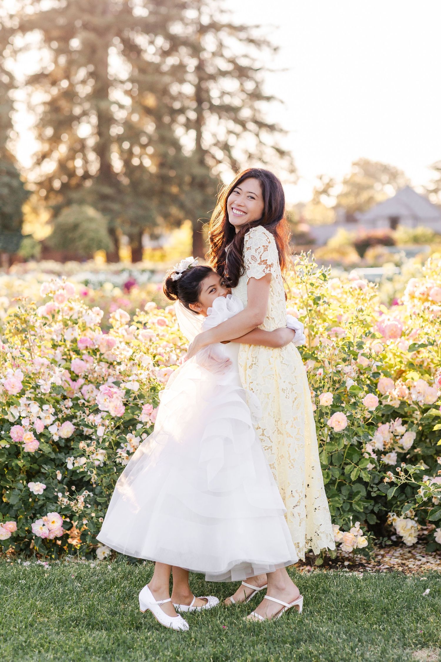 A mother and daughter share tender moments in a blooming rose garden at sunset.