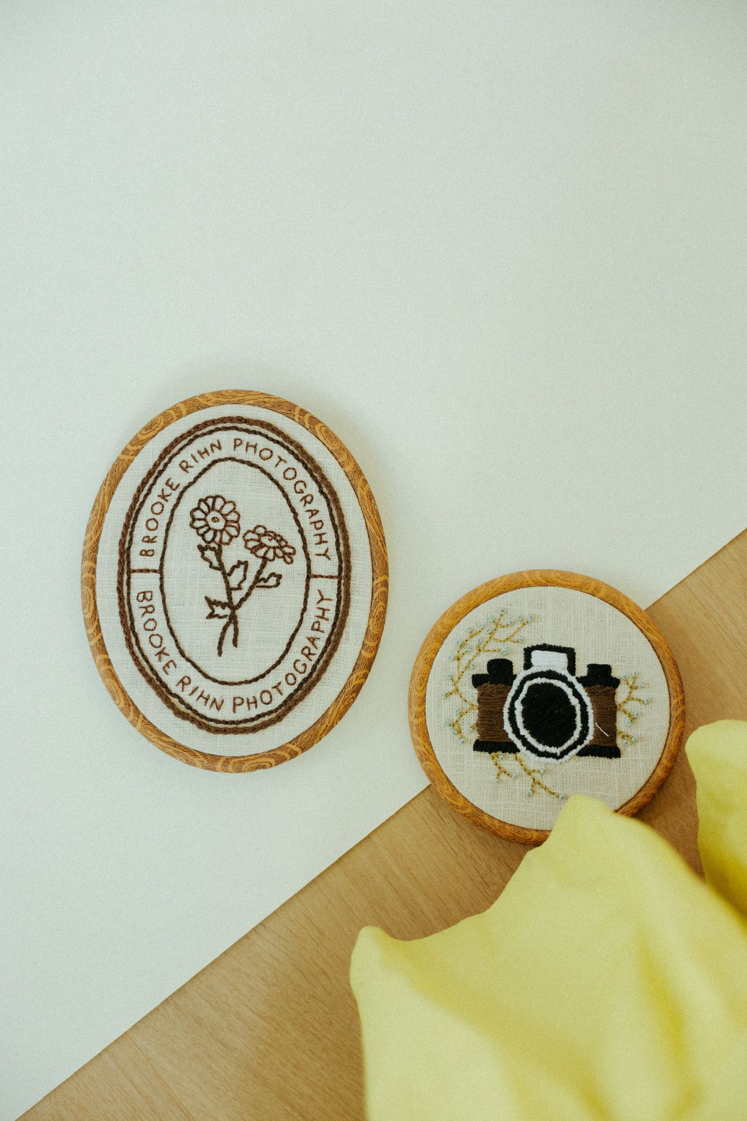 Two decorative round cork stamps featuring a floral design and camera icon rest on a wooden surface with yellow fabric.