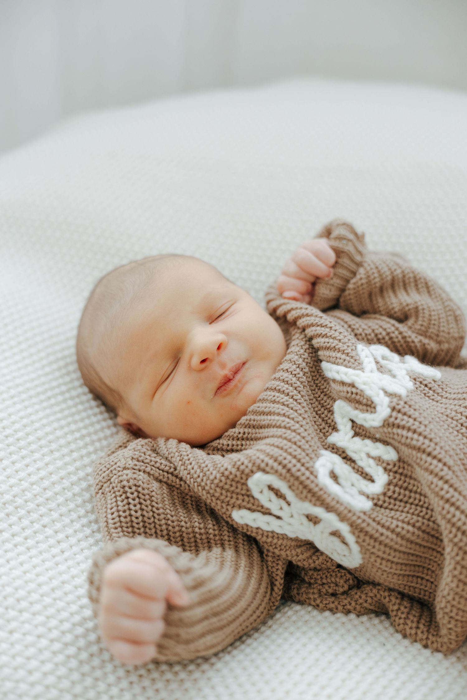 Sleeping infant in cozy brown knit sweater on white blanket.