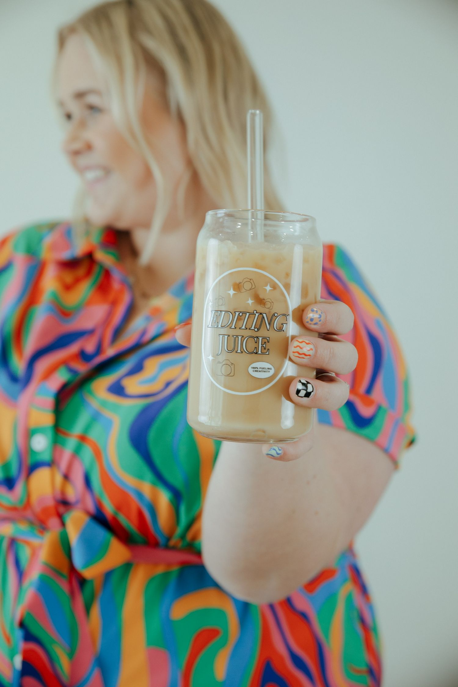 A colorful drink in clear cup with straw held up against bright patterned background.