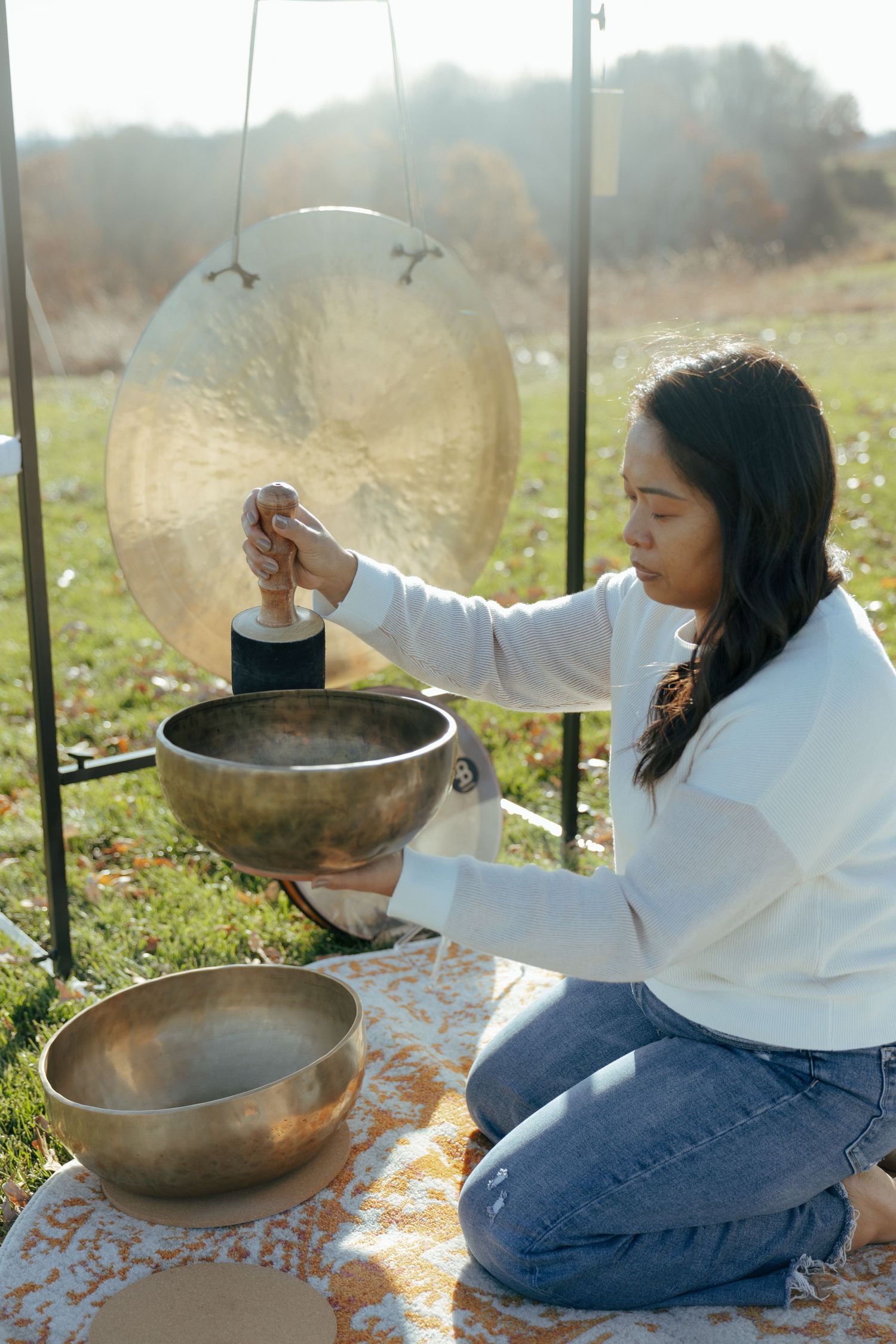 Person in white sweater playing meditation bowls outdoors.