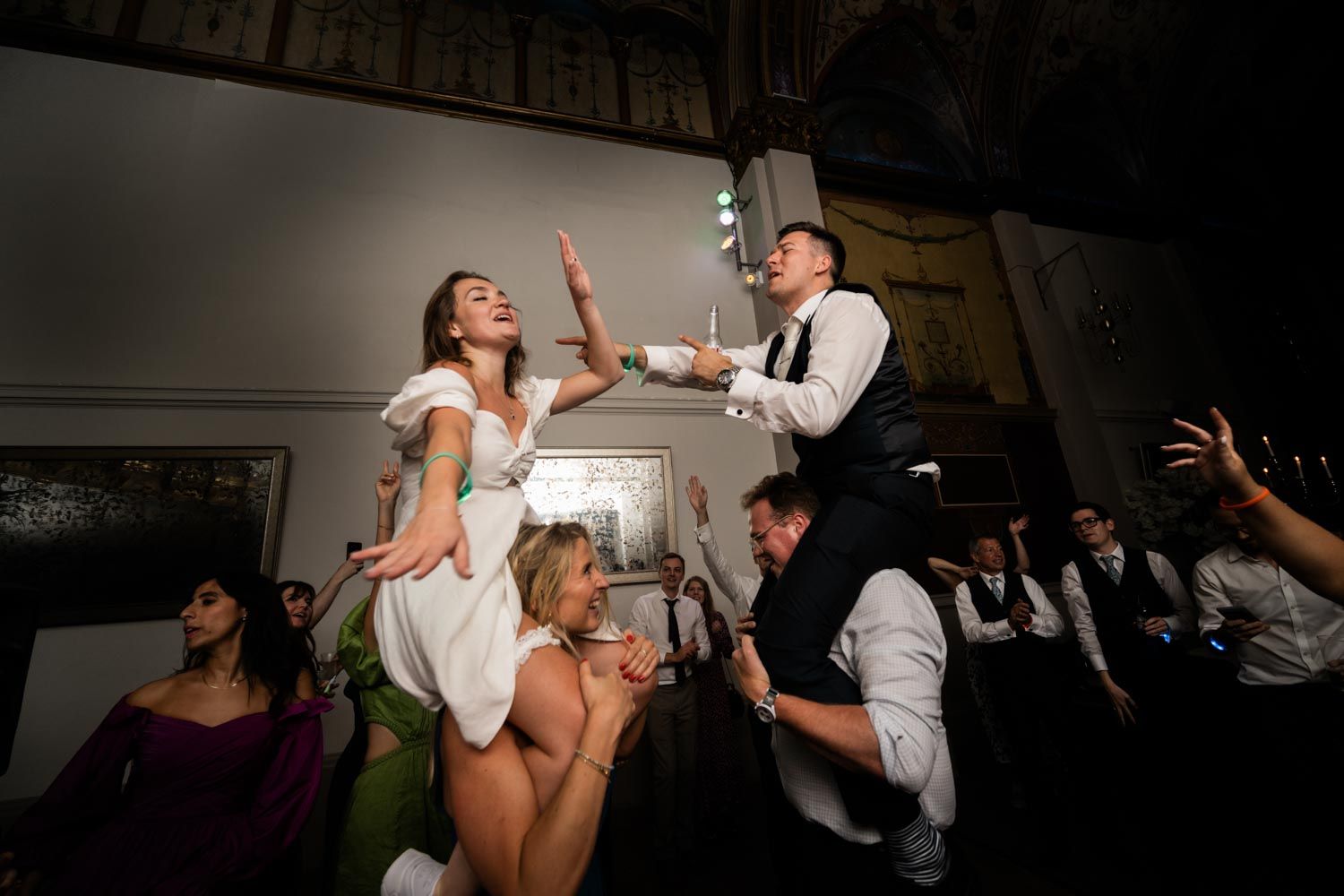 Lively wedding reception dance party with bride and groom being lifted up by guests on the dance floor.