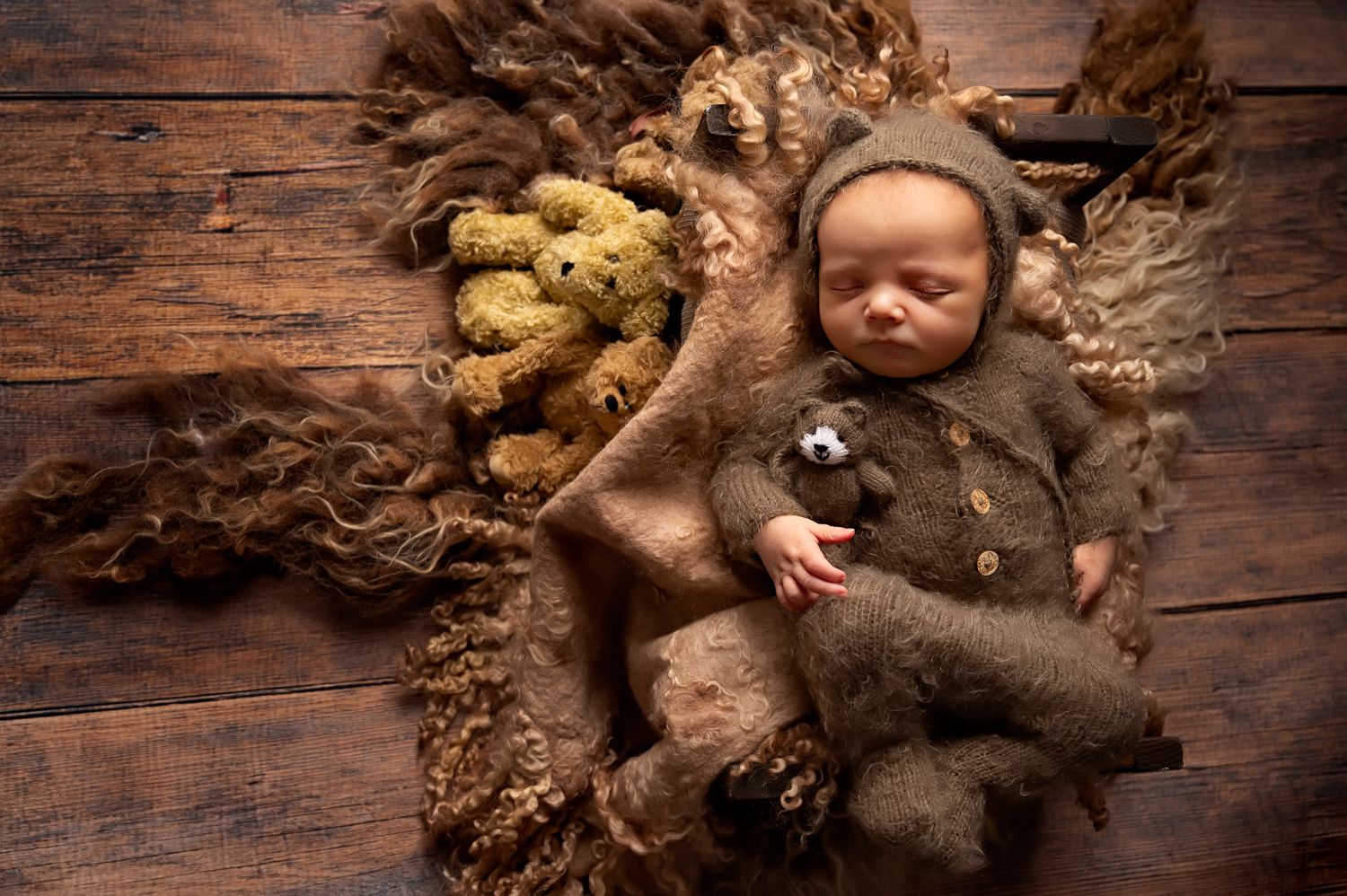 Newborn in brown bear costume sleeping on wooden backdrop with autumn decorative elements and furry textures.