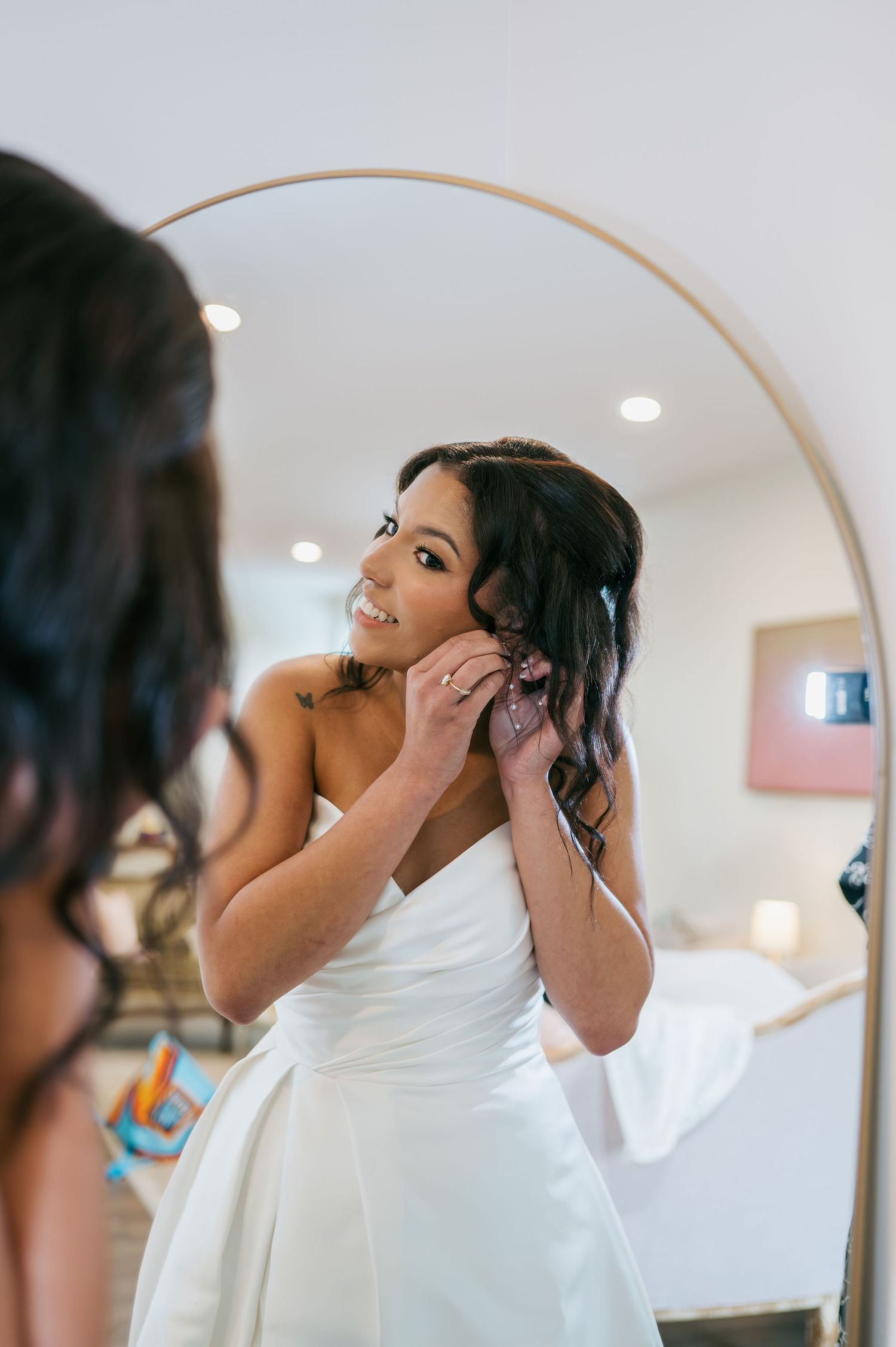 Bride putting on earrings while looking in a round mirror on her wedding day, wedding photographer North Carolina