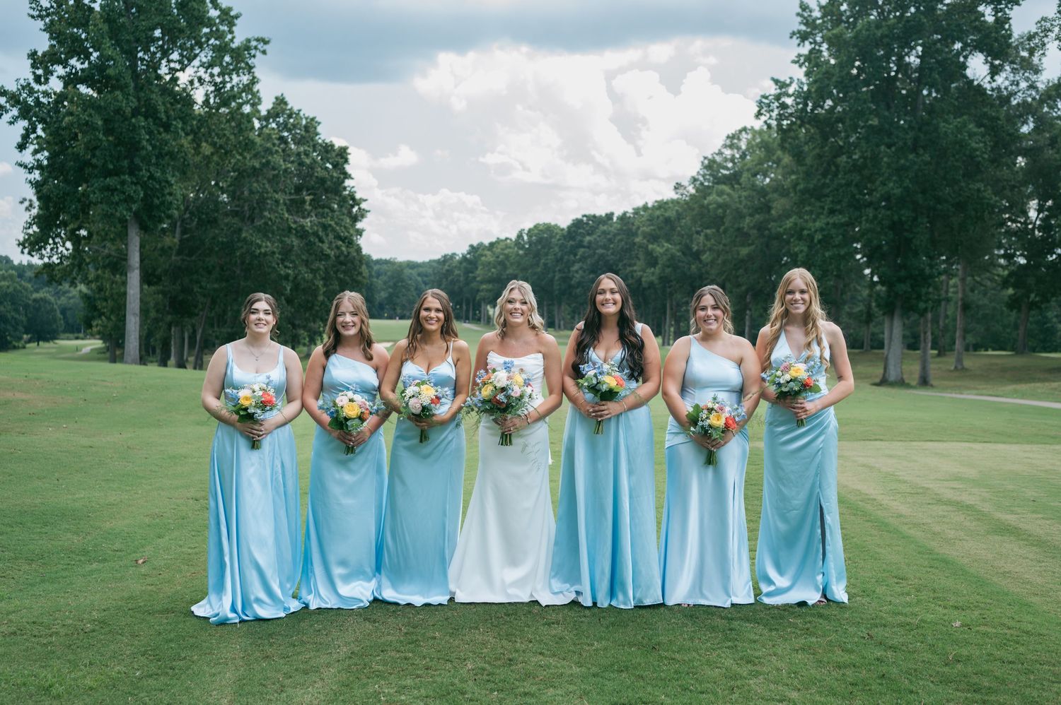 Bride with six bridesmaids in light blue gowns holding bouquets on green golf course,  wedding photographer Asheboro NC