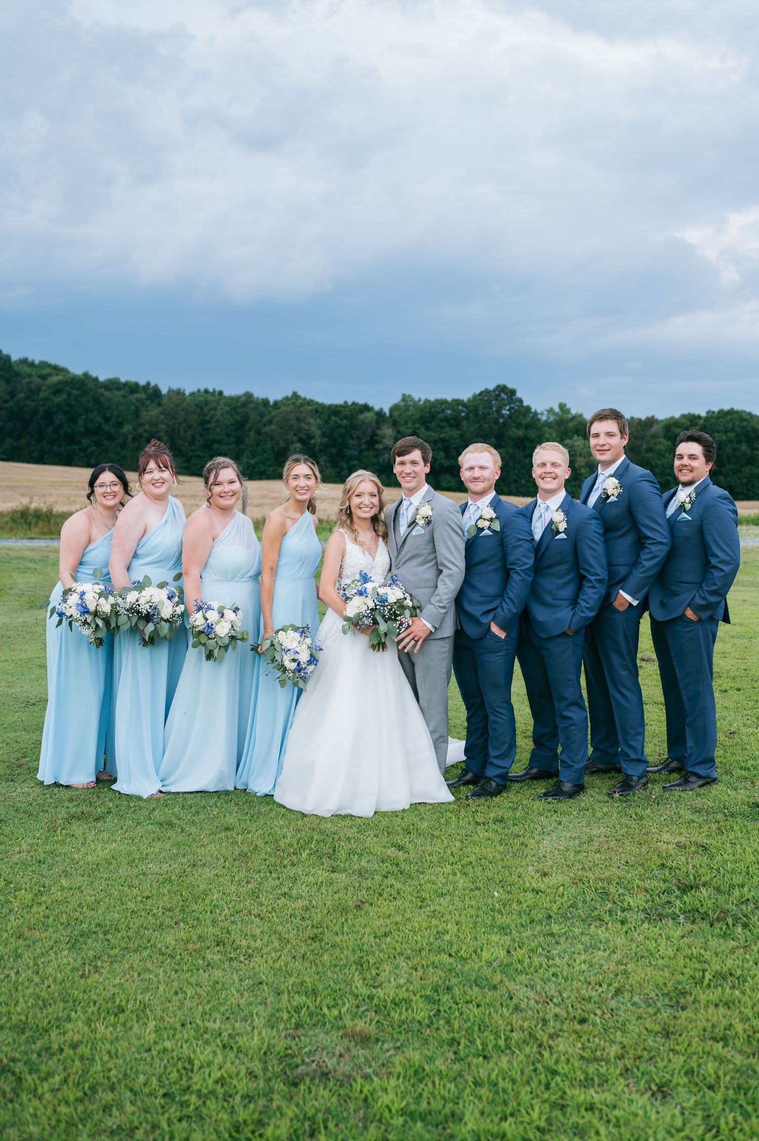 Wedding party with bridesmaids in blue and groomsmen in navy suits on green field, wedding photographer North Carolina