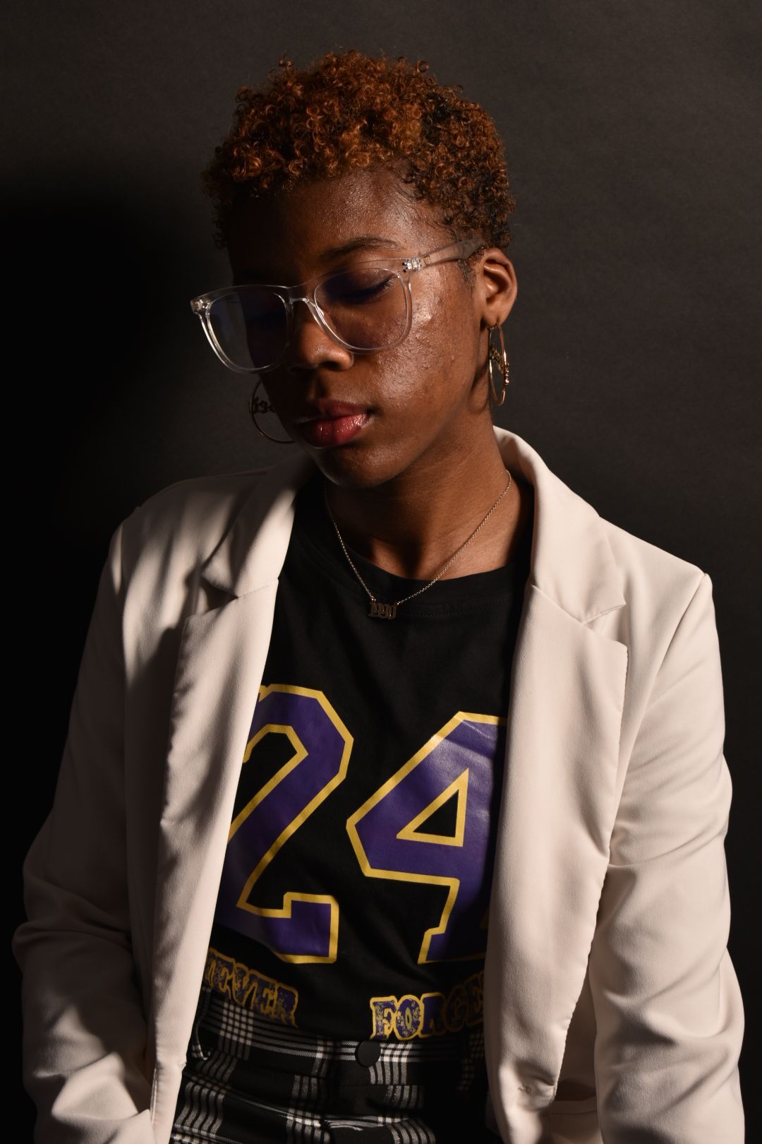 Young woman in white blazer and number 24 jersey with clear glasses poses confidently in studio.