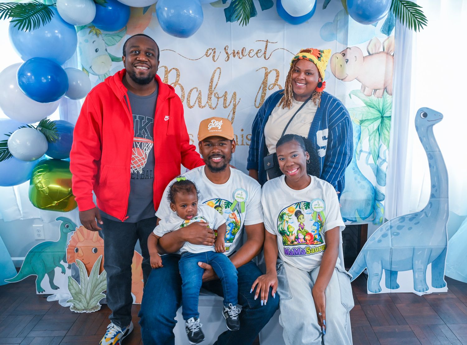 Group of five people posing together in front of a Baby Boy balloon backdrop at a shower.