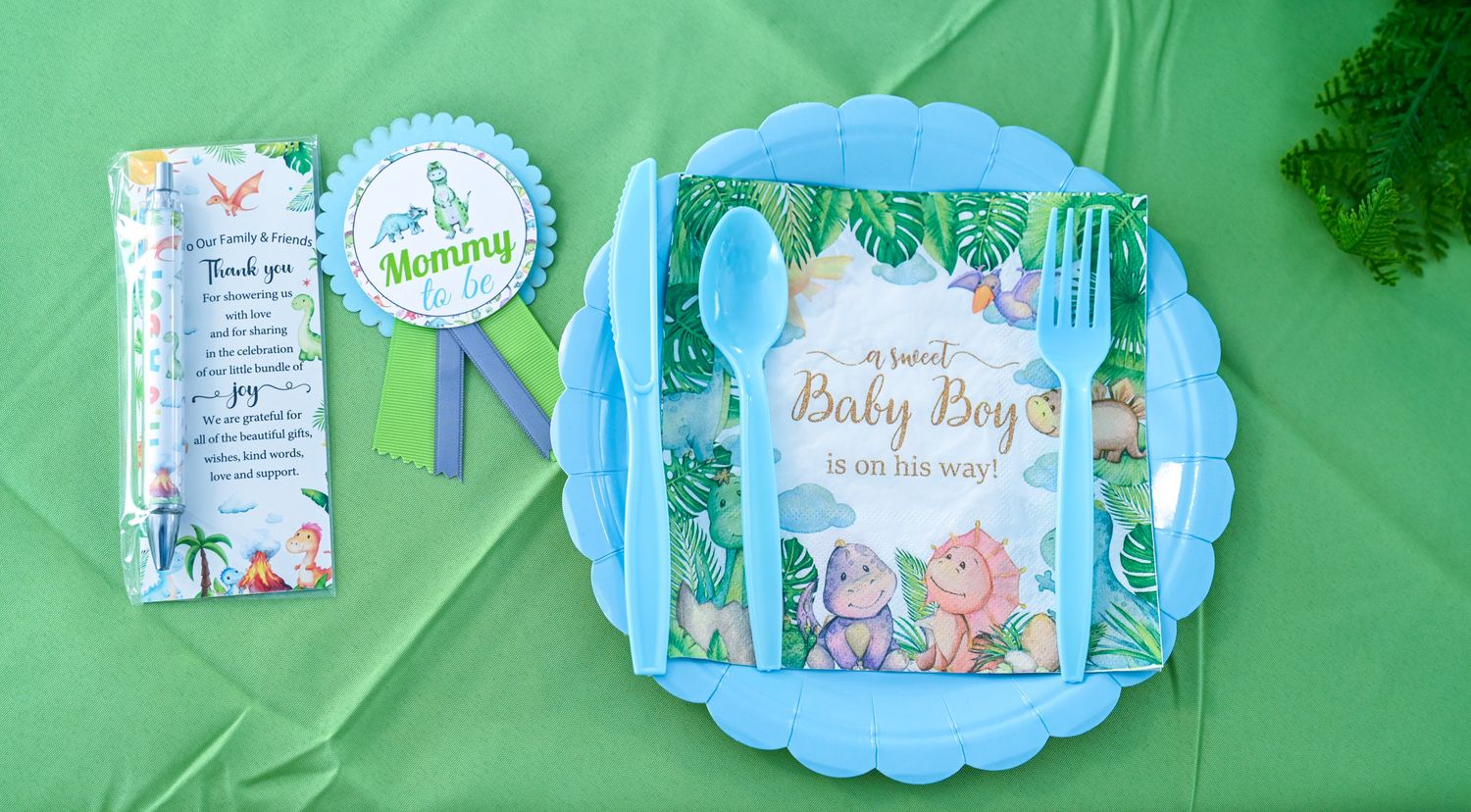 Mommy baby boy dinosaur shower place setting with blue plate, utensils, and ribbon badge.