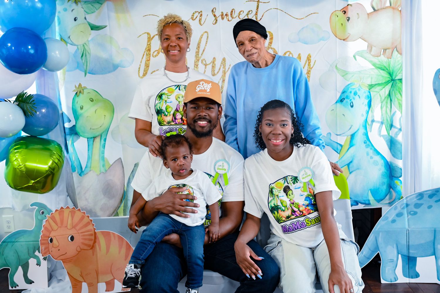 Five family members posing at a sweet baby boy dinosaur-themed birthday party.