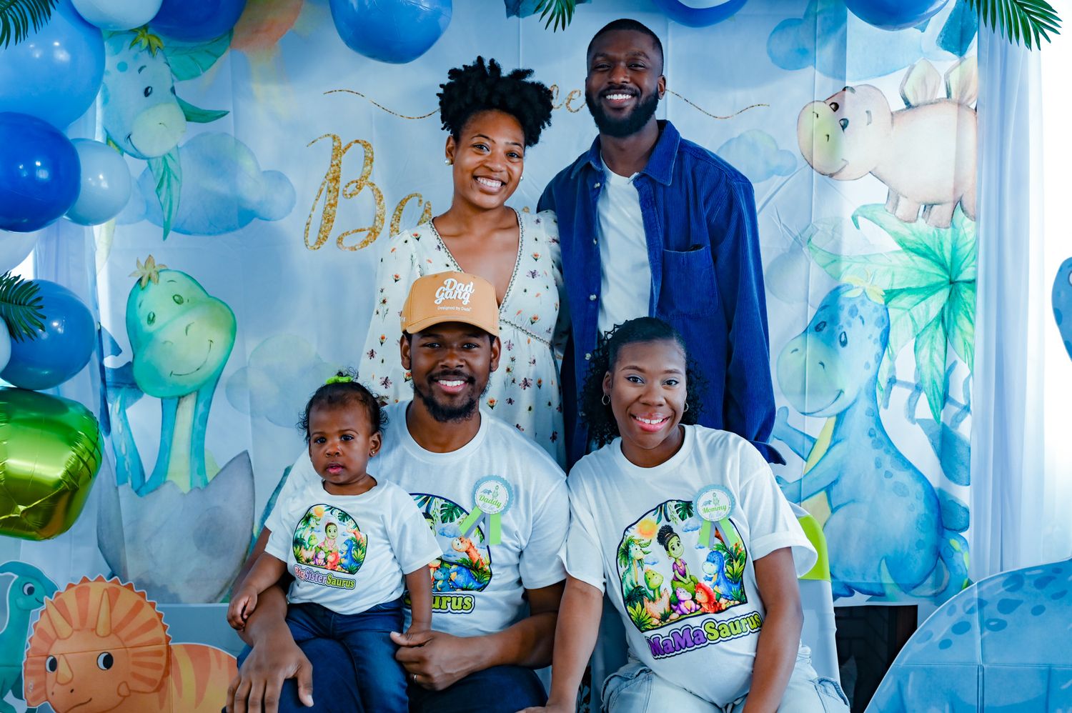 Family posing together at a dinosaur themed baby shower with blue and green balloon decorations.