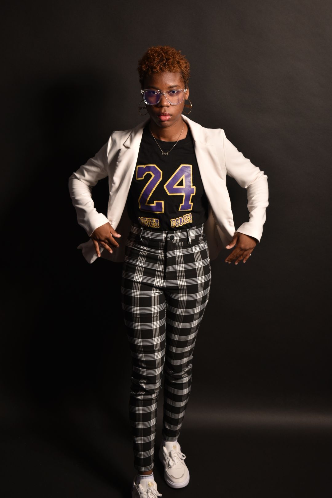 Confident woman in white blazer, number 24 jersey, and plaid pants poses with hands on hips.
