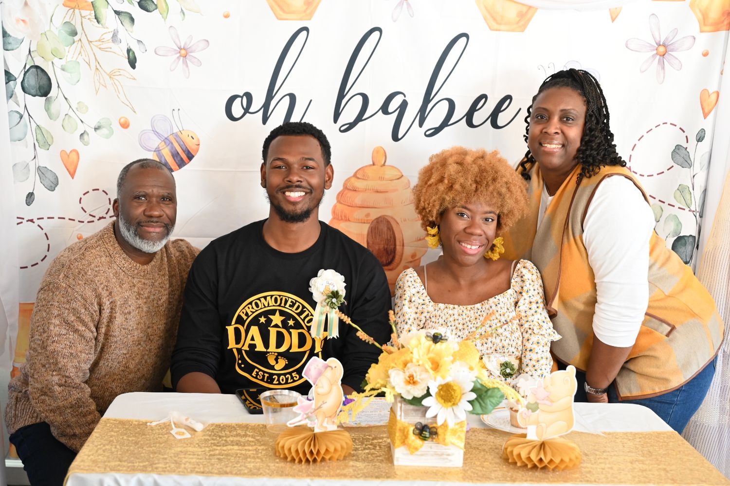Four family members posing at an oh babee baby shower with sunflower and honeycomb decor.