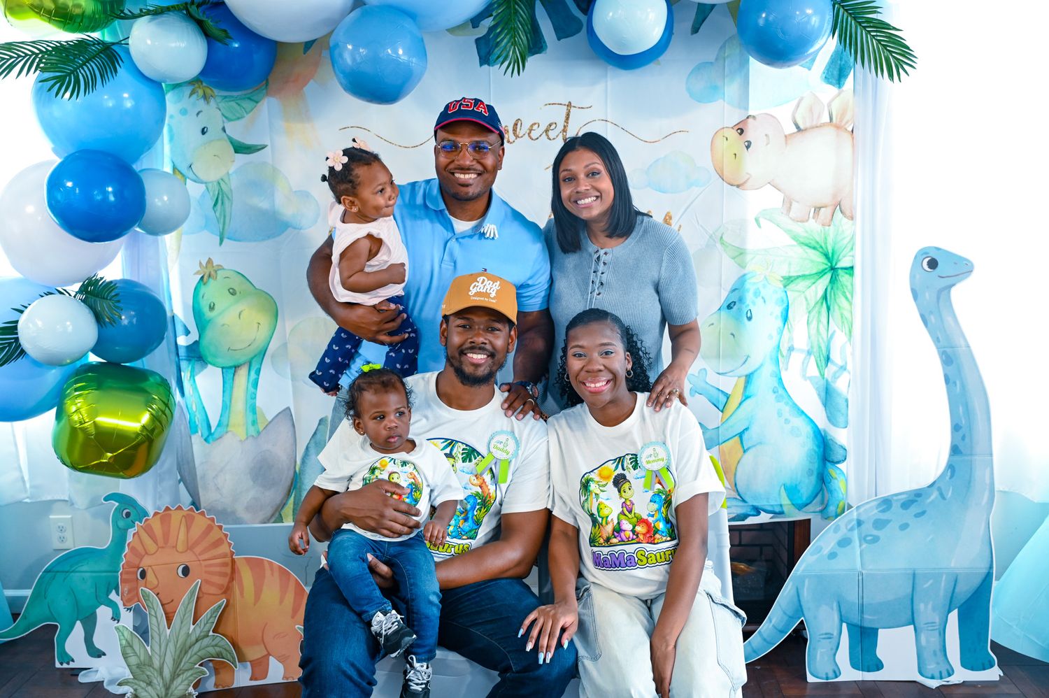 Group of seven celebrating at a colorful dinosaur baby boy party with blue balloons.