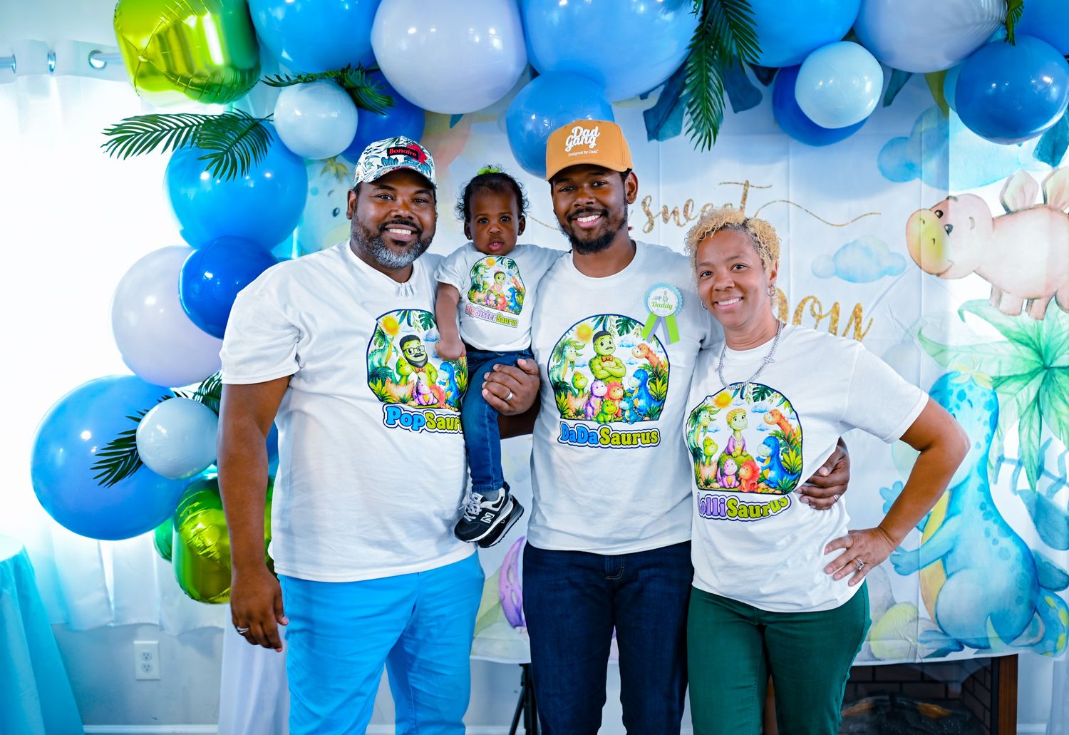 Group of four posing with a toddler at a colorful tropical themed celebration with balloons.