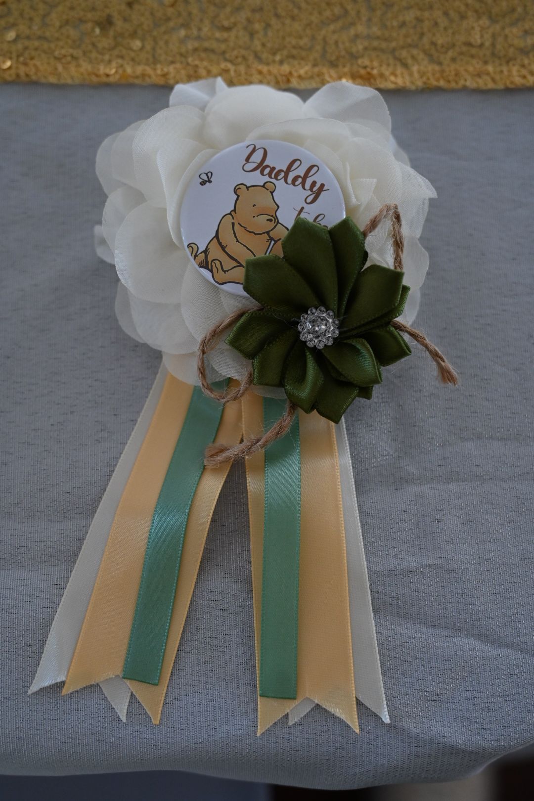 Daddy to be Winnie the Pooh ribbon corsage with white flowers, green accent, and yellow ribbons.