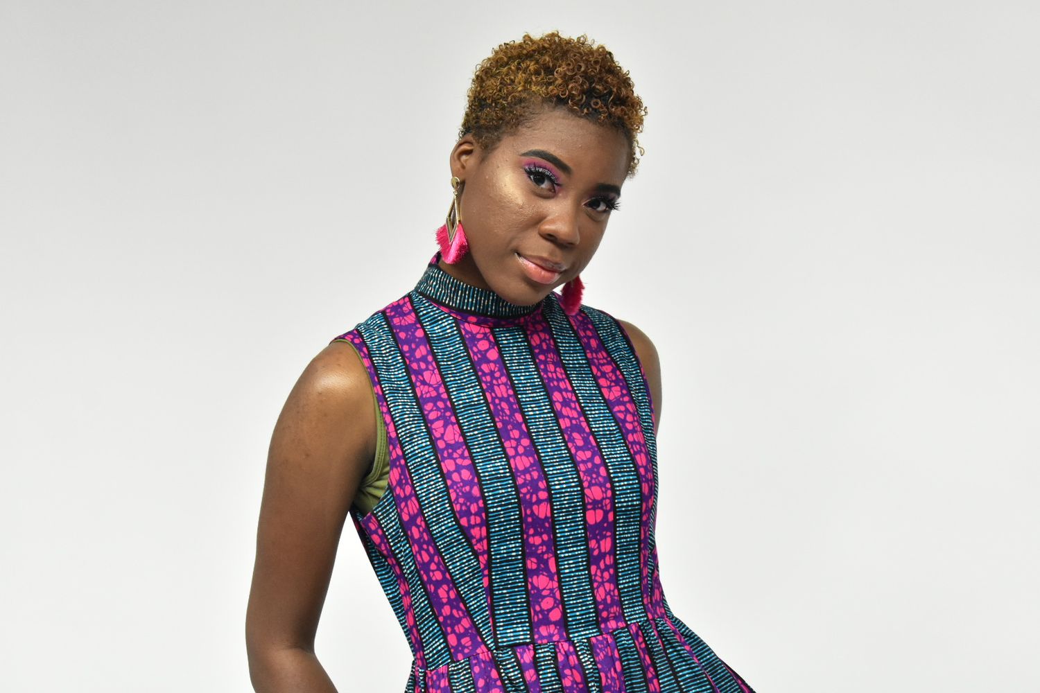Woman in vibrant teal and pink African print sleeveless dress posing on white background.