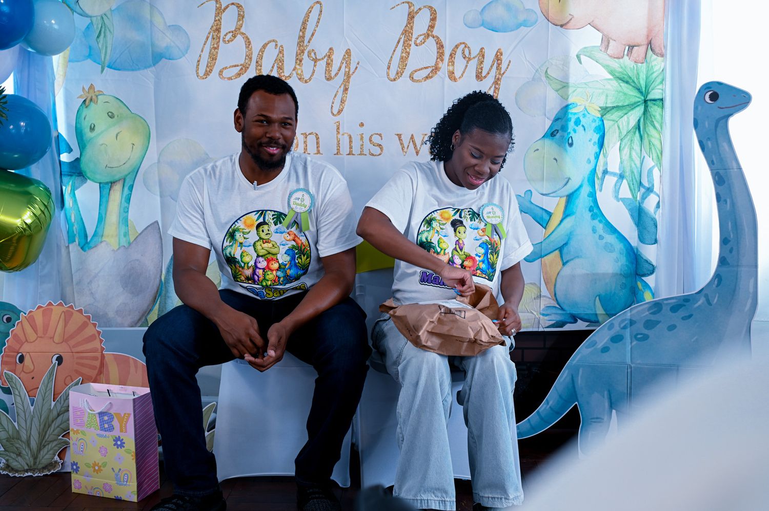 Couple in matching shirts sitting together opening gifts at a Baby Boy baby shower.