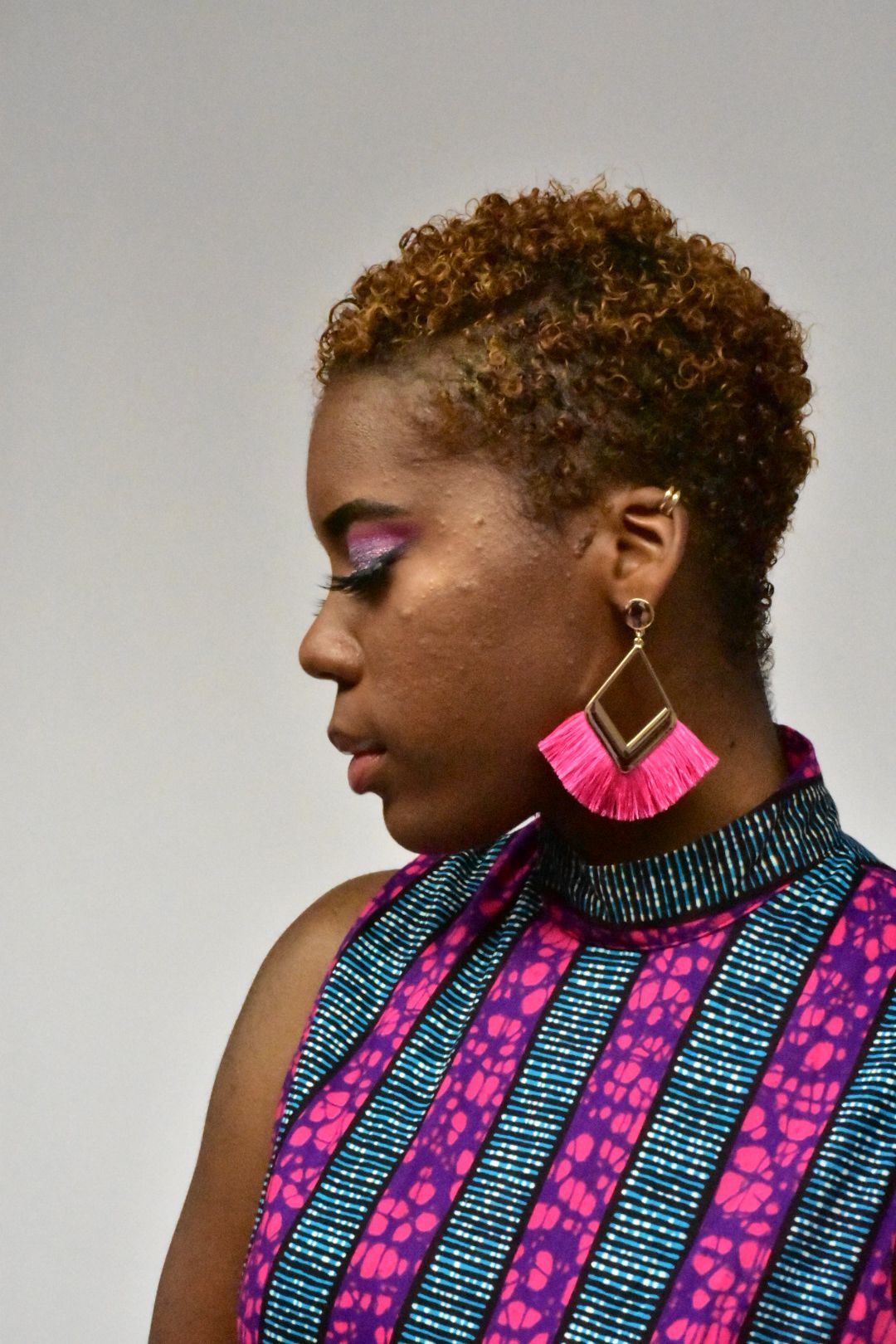 Side profile of woman with curly hair wearing pink geometric tassel earrings and African print top.