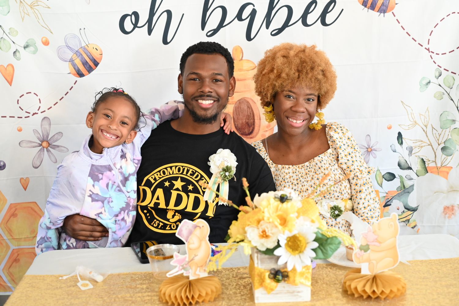 Man in Promoted to Daddy shirt poses with woman and young girl at oh babee baby shower.