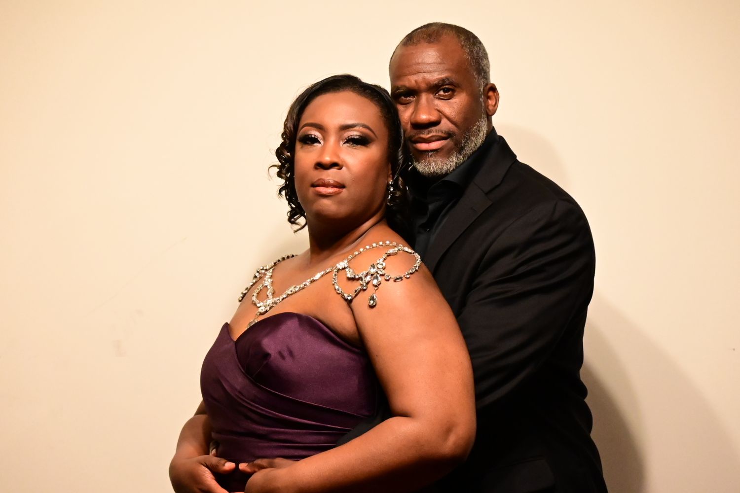 Elegant couple posing together, woman in purple gown and man in black suit.
