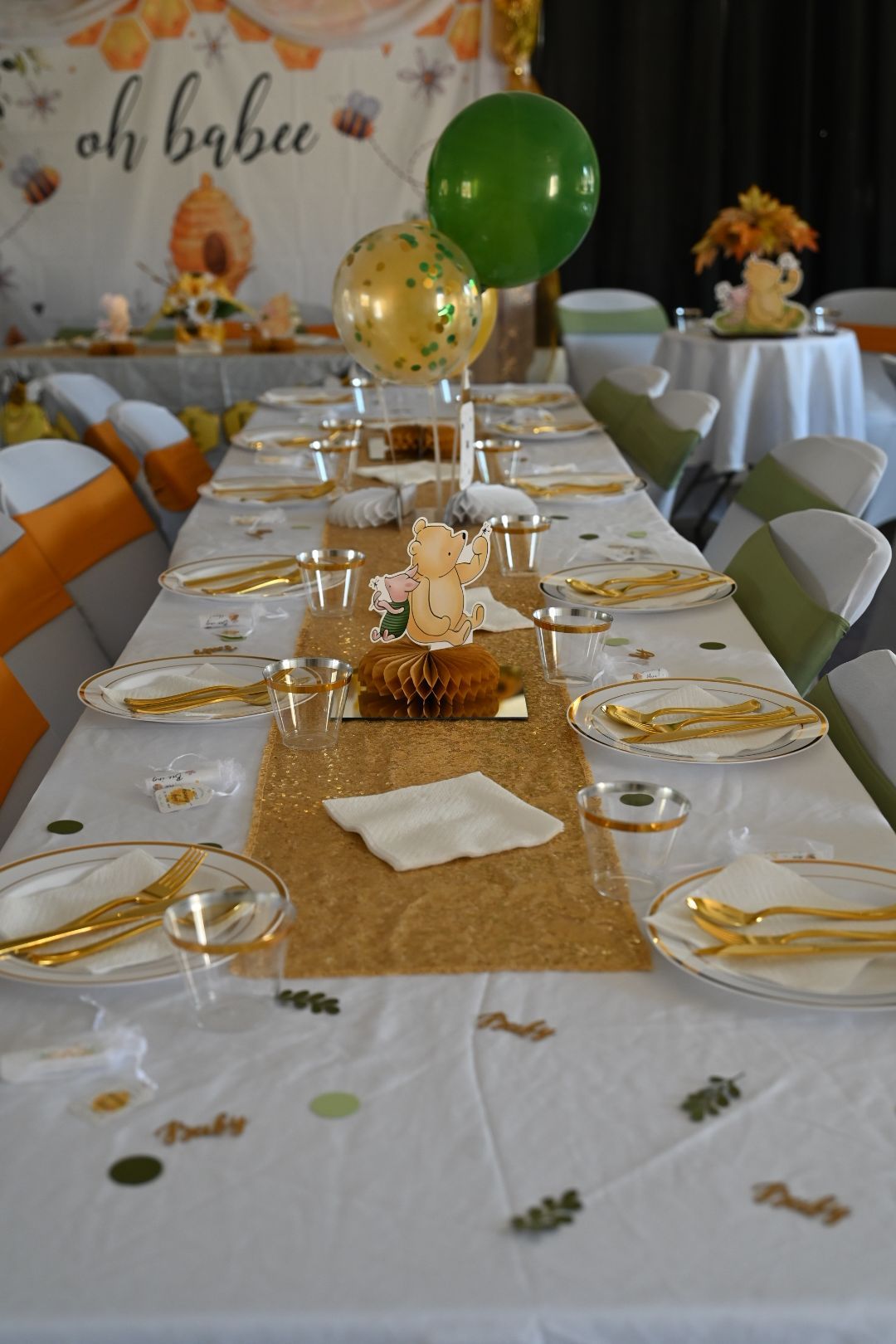 Honey bee baby shower table decorated with gold sequin runner, Winnie the Pooh centerpiece, and green balloons.