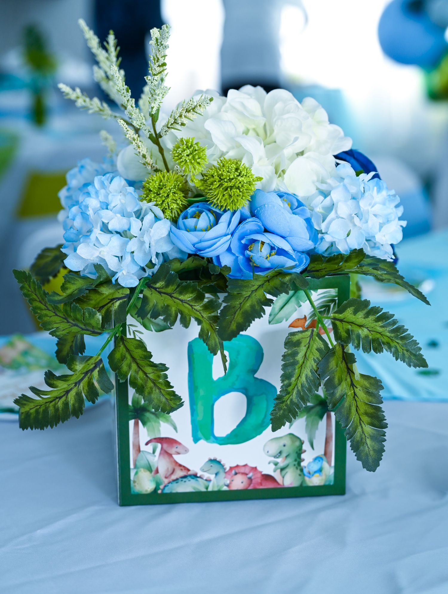 Baby boy shower floral centerpiece with blue hydrangeas in a dinosaur-printed box with letter B.