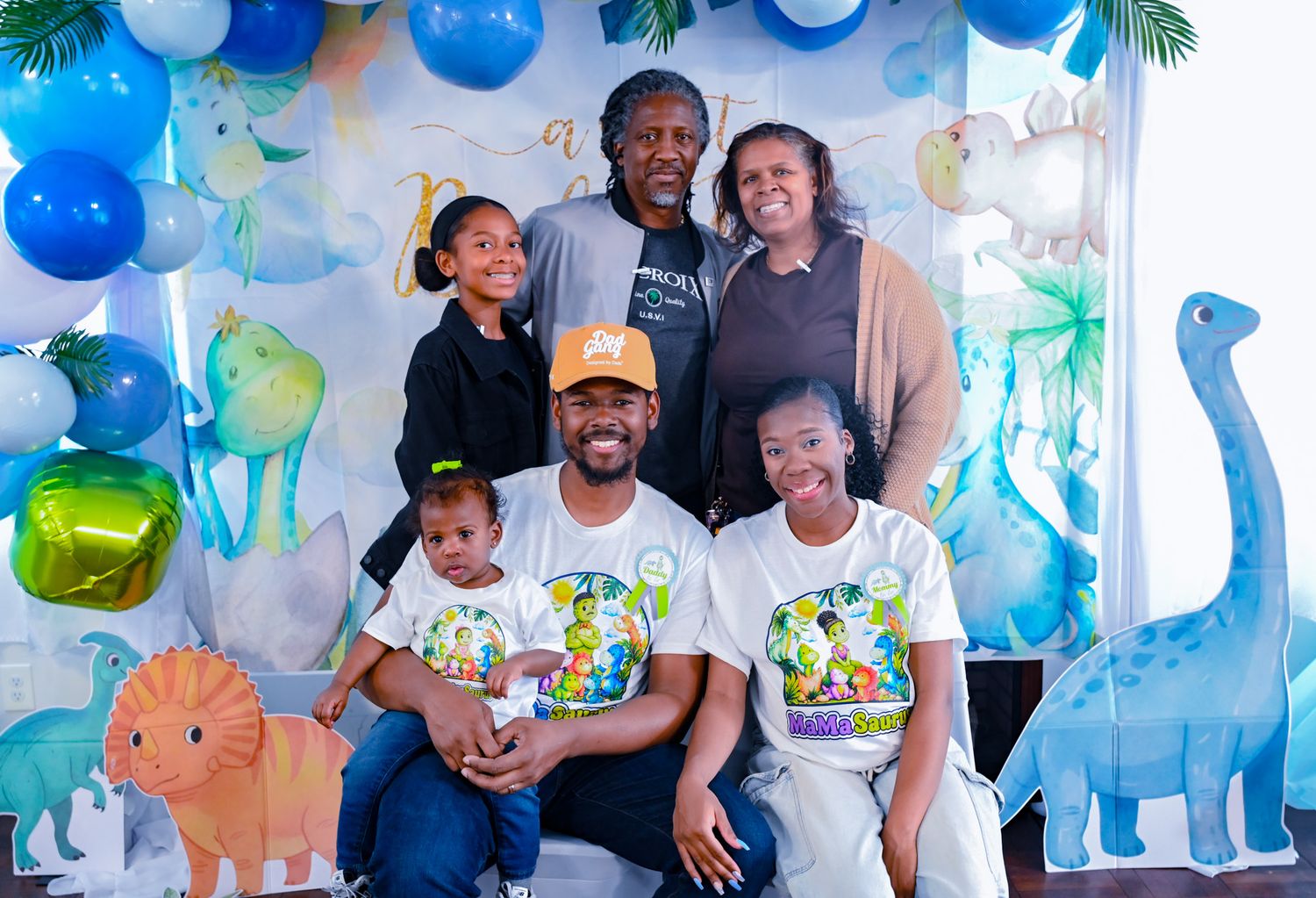 Seven family members posing together at a dinosaur-themed baby boy birthday party.
