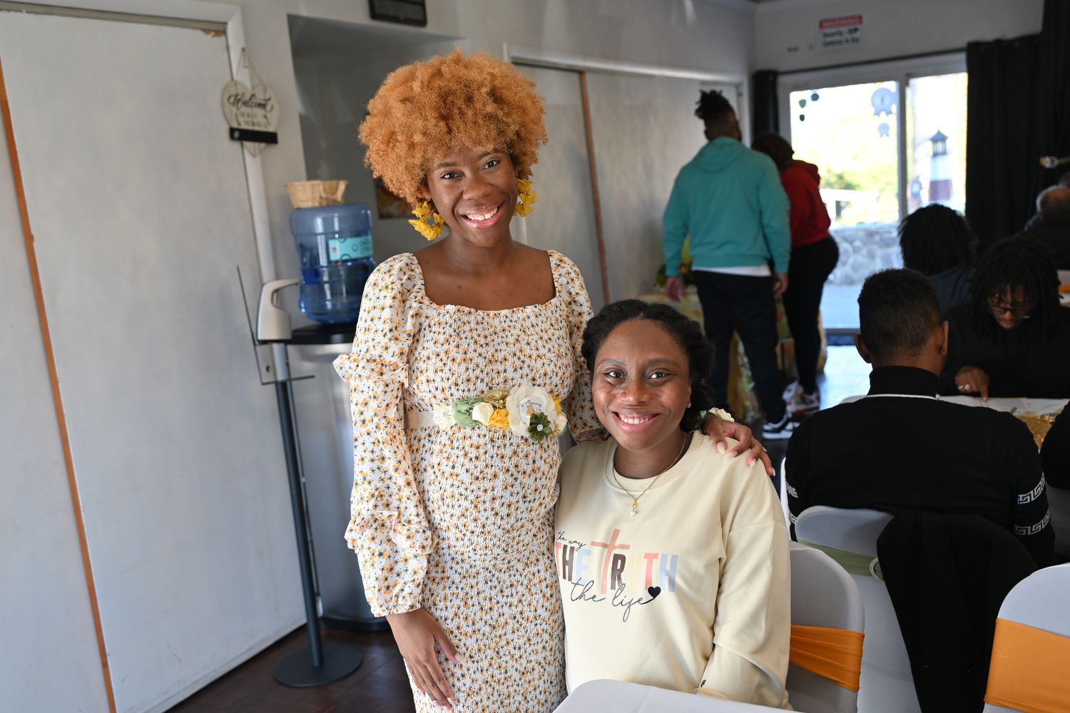 A smiling woman in a floral dress poses with a young girl at a cheerful baby shower event.