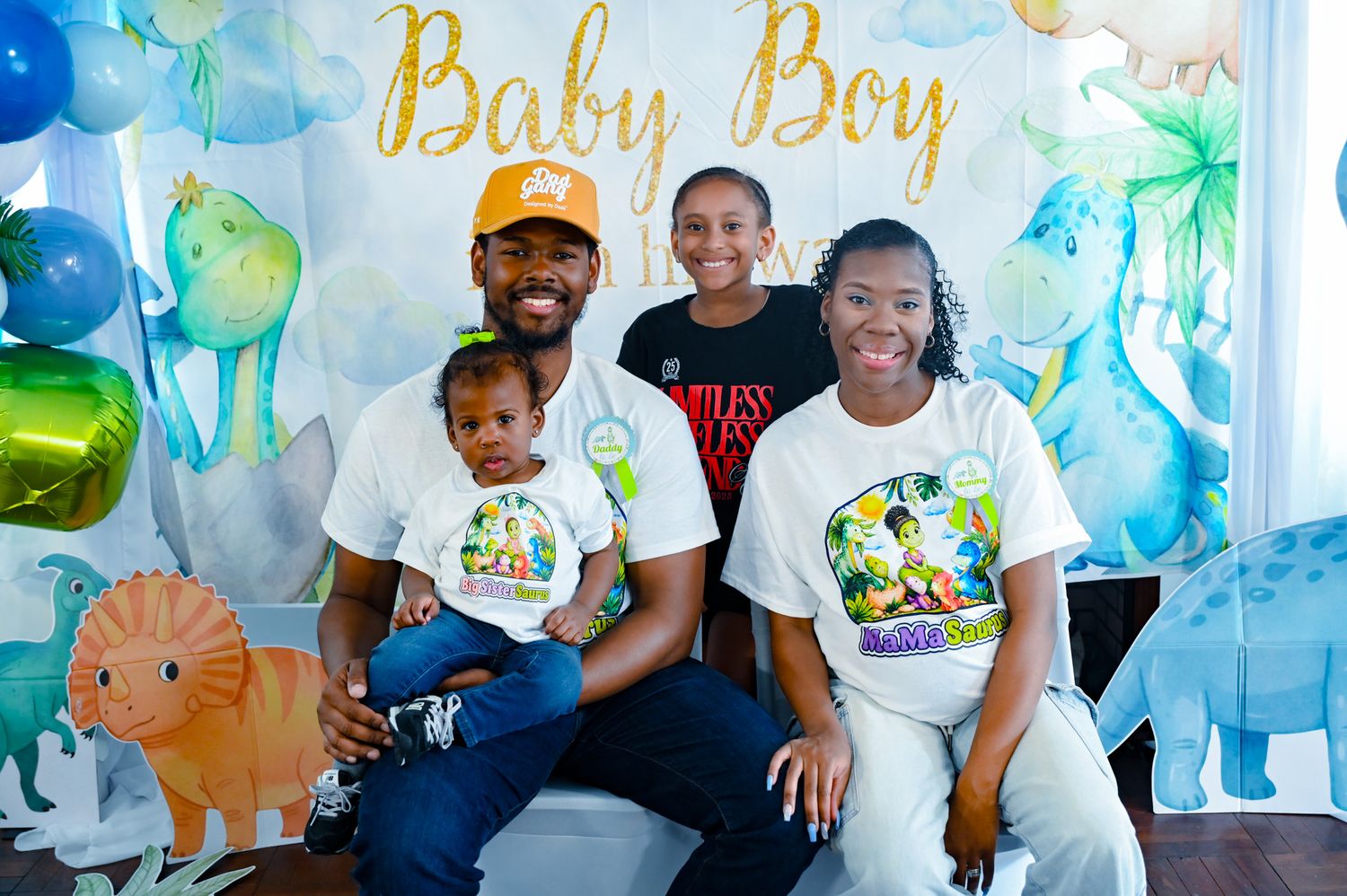 Family posing under Baby Boy banner at a dinosaur-themed birthday party celebration.