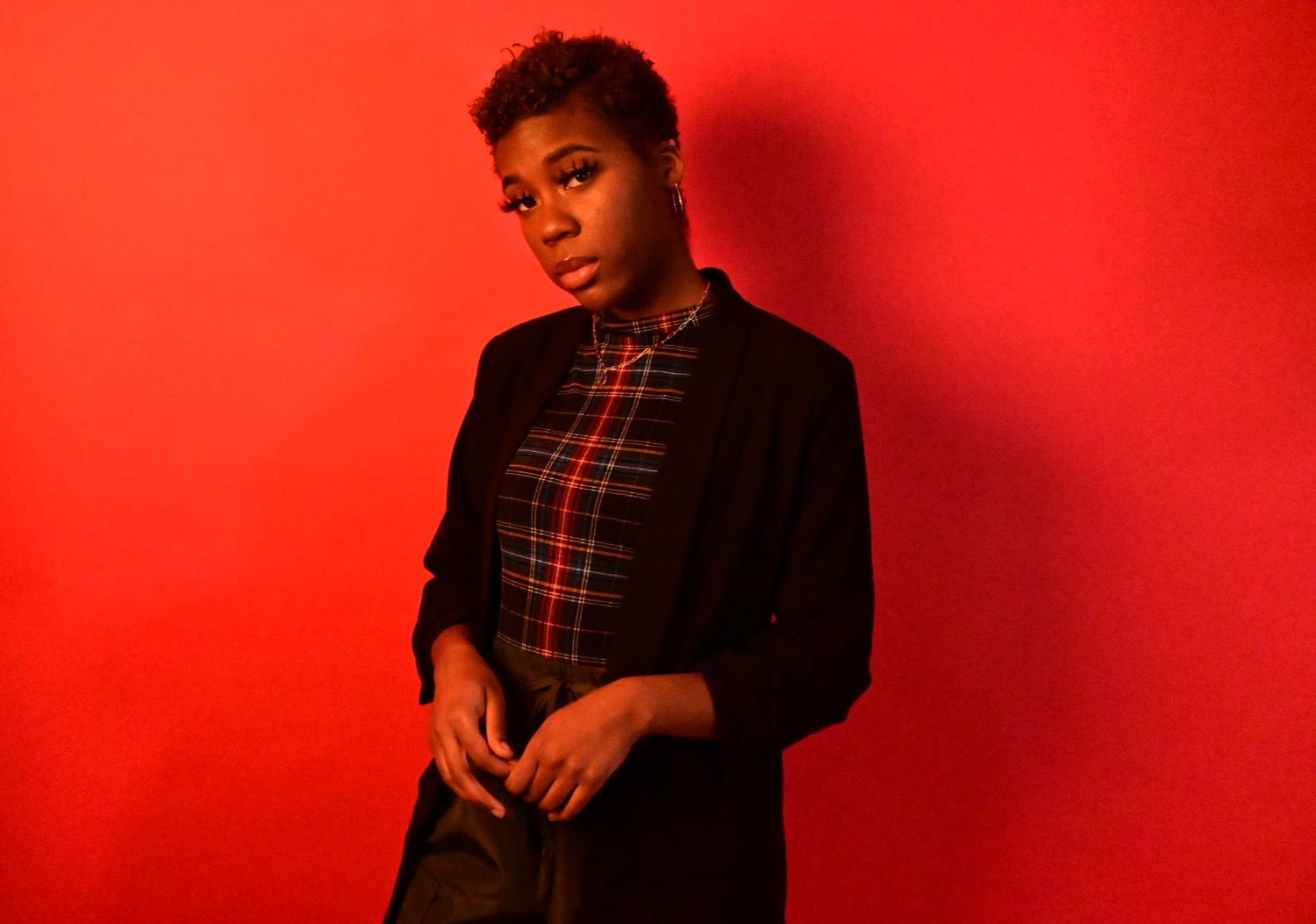 Woman in plaid shirt and black blazer looking sideways against a red background.