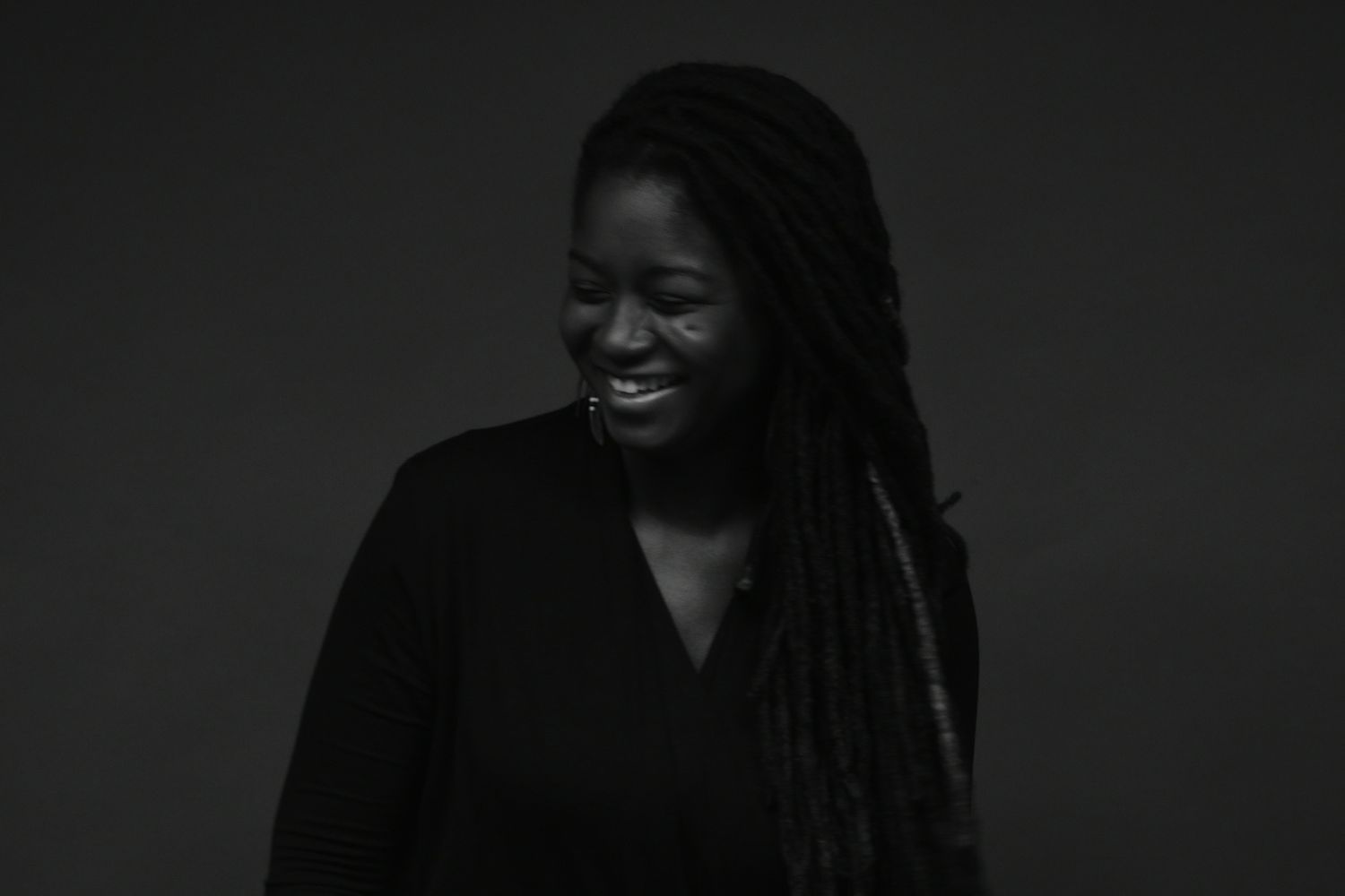 Black woman with long locs laughs joyfully in black and white portrait photo.