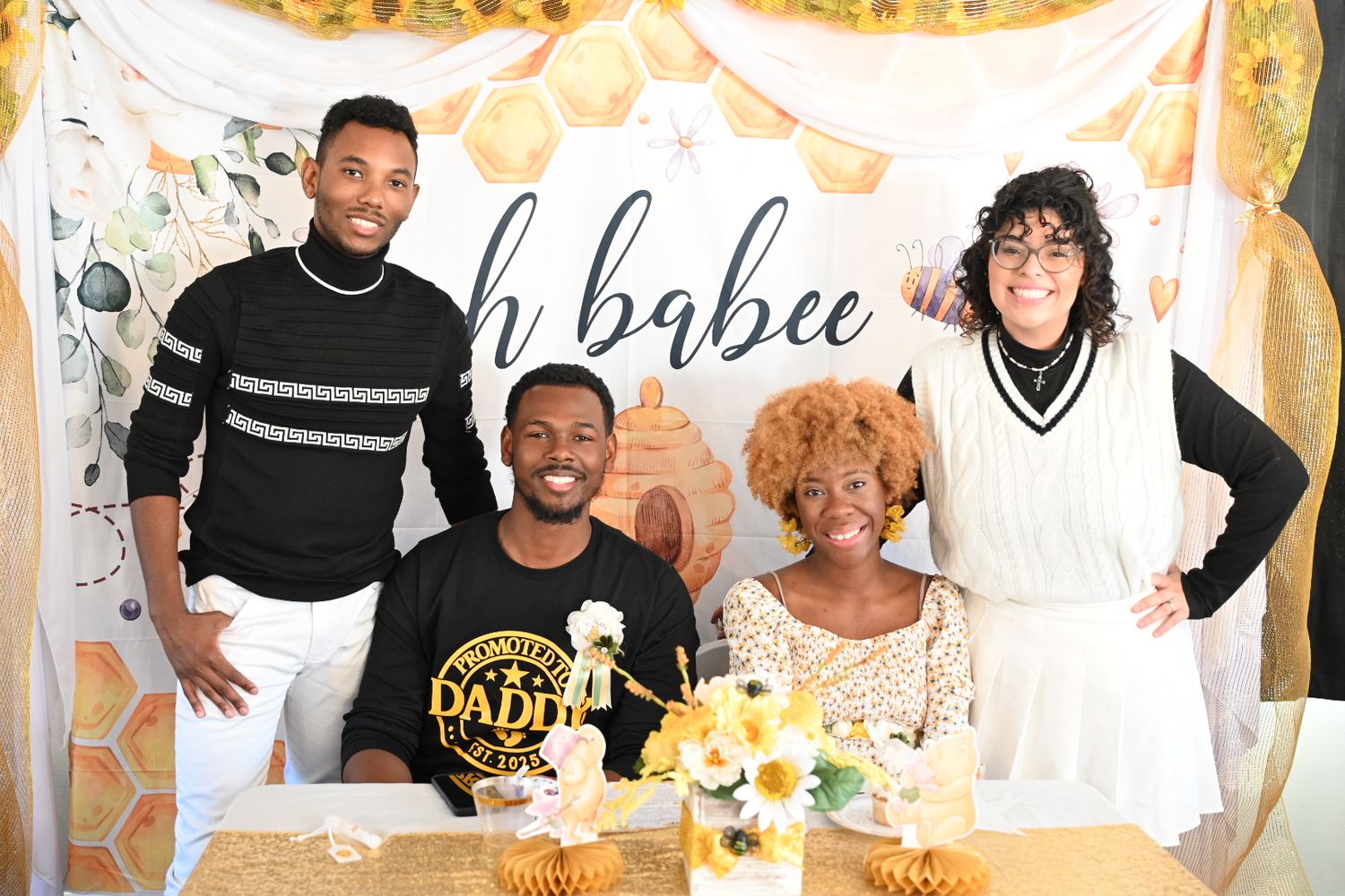 Four guests smiling at an oh babee baby shower with yellow sunflower centerpieces and decorations.