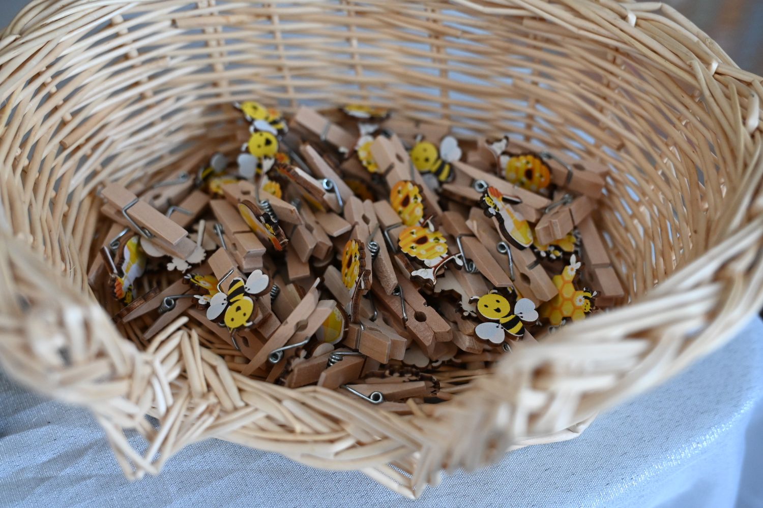 Wicker basket filled with wooden mini clothespins decorated with yellow bee designs for baby shower game.