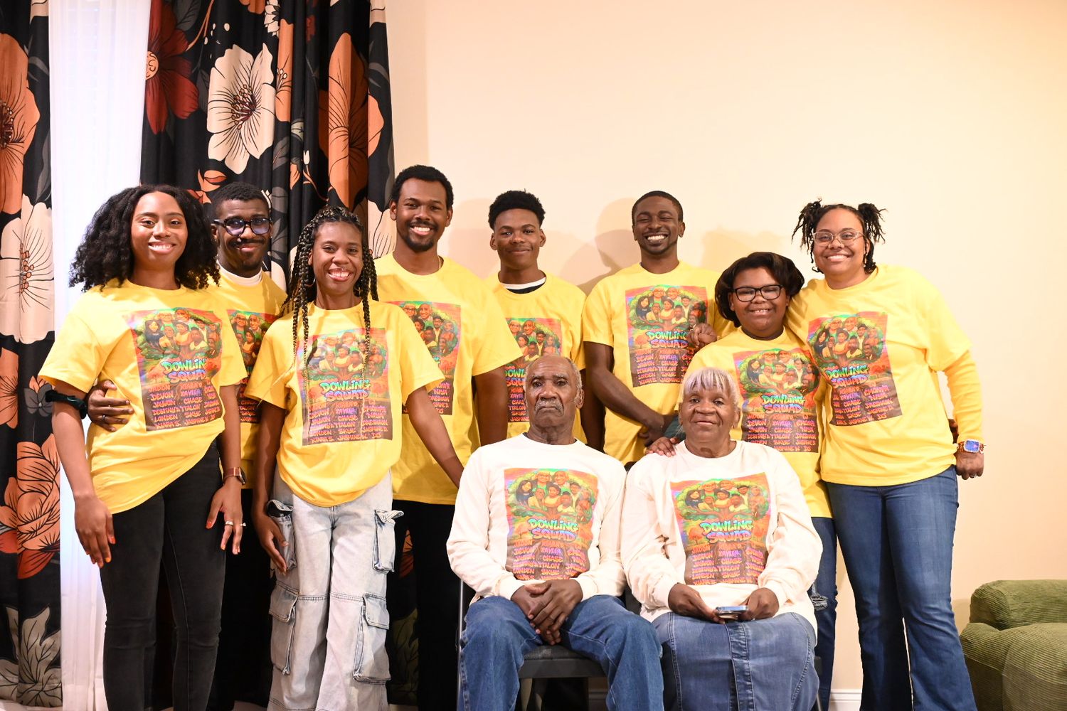 Family group photo with eleven members wearing matching yellow shirts, two elders seated in foreground.