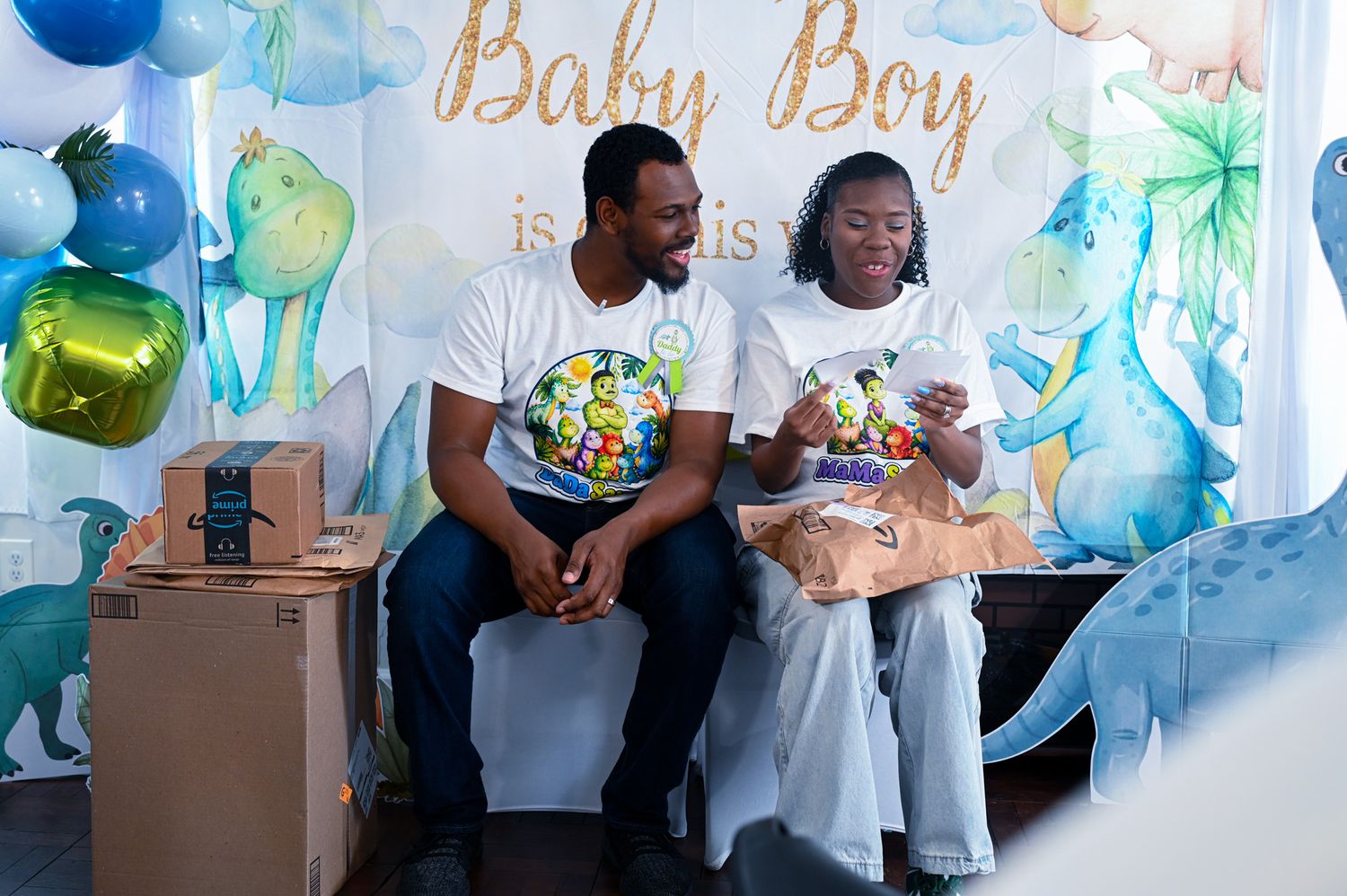 Couple sharing a joyful moment while unwrapping baby gifts at a decorated Baby Boy shower.