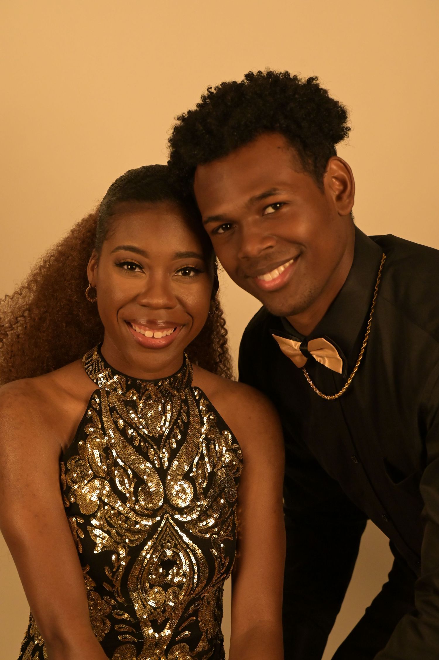 Smiling young couple posing together in formal attire against a warm golden background.