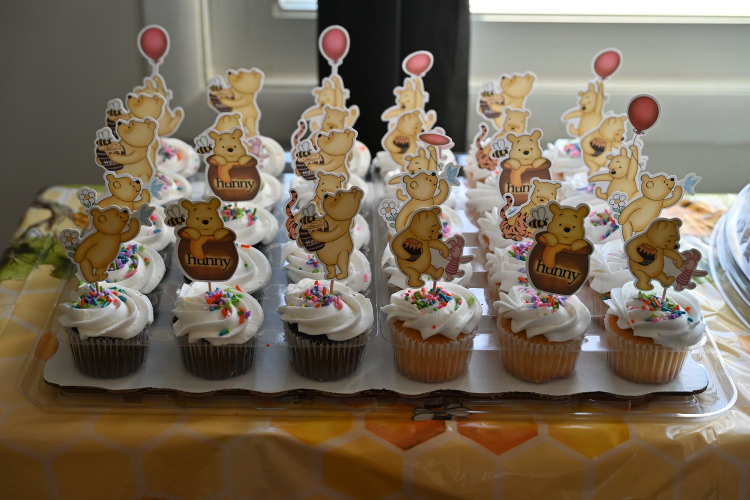 Tray of white frosted cupcakes topped with Winnie the Pooh character cake toppers for a baby shower celebration.